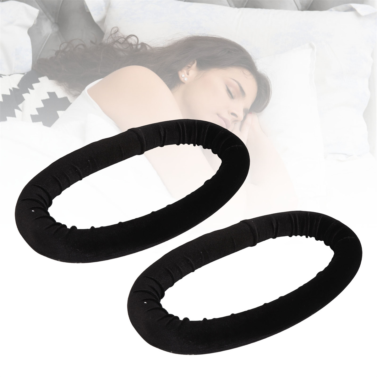 Zwei schwarze Haarroller auf einem Bett. Eine Frau schläft im verschwommenen Hintergrund.
