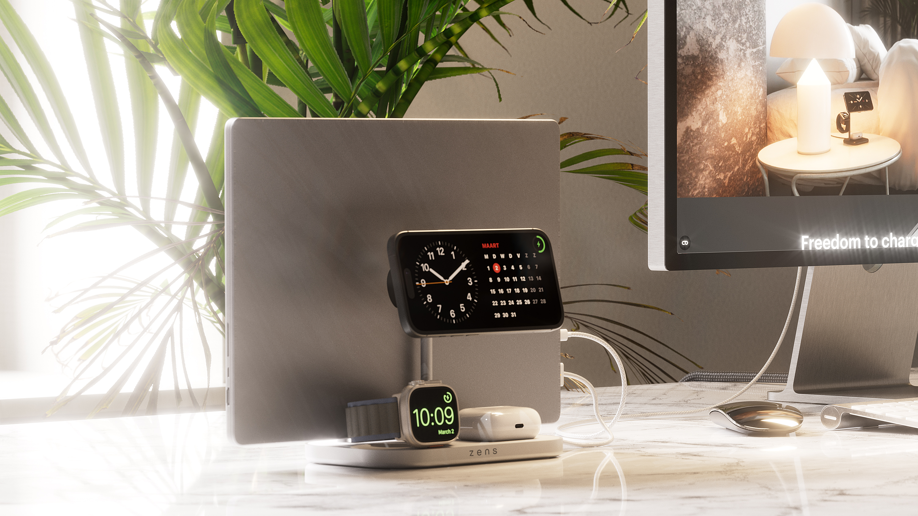 Ein Schreibtisch-Setup mit Laptop, Uhr, Telefon und Kopfhörern, die geladen werden. Ein Monitor mit Bild.