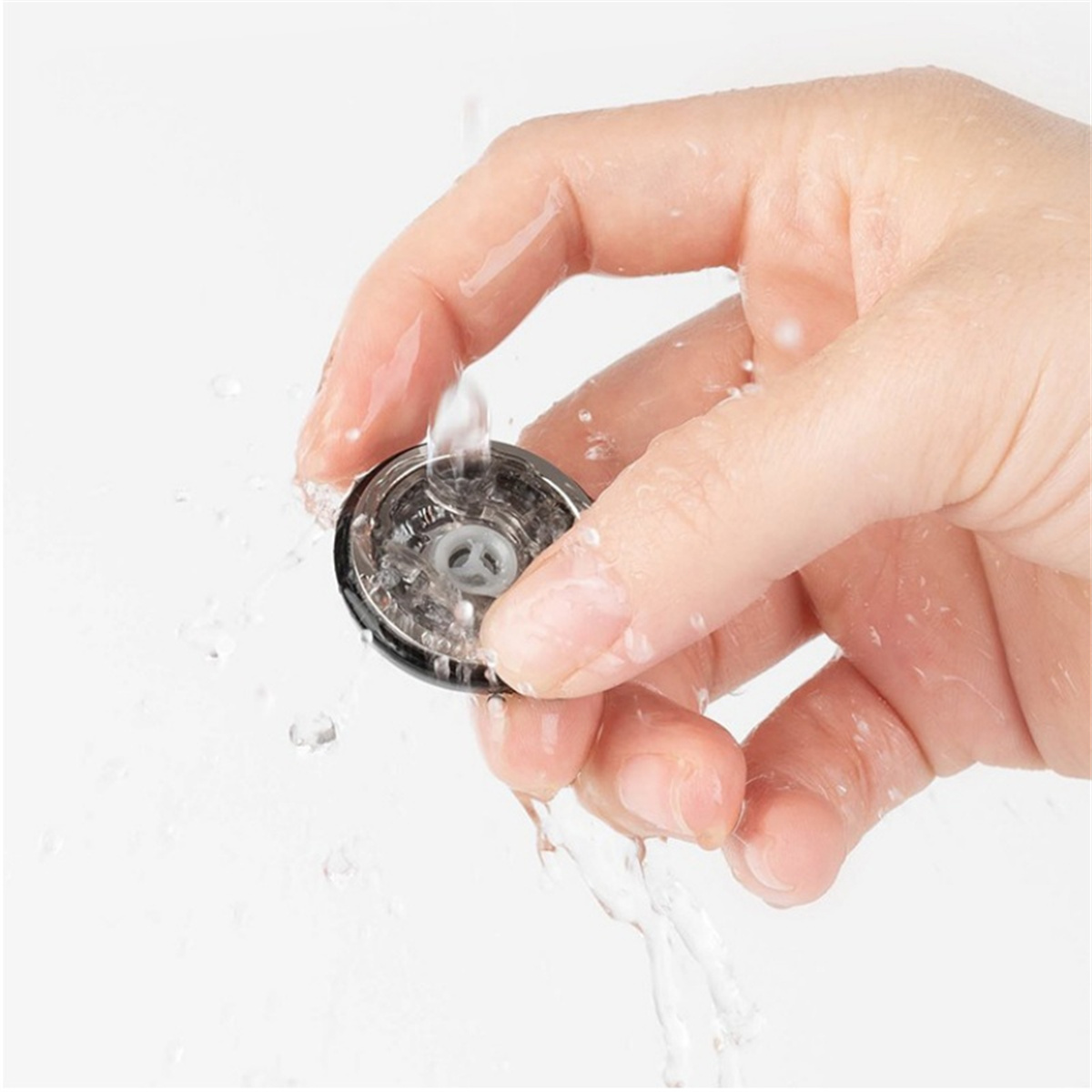 Hand gießt Wasser auf ein schwarz-silbernes Objekt.