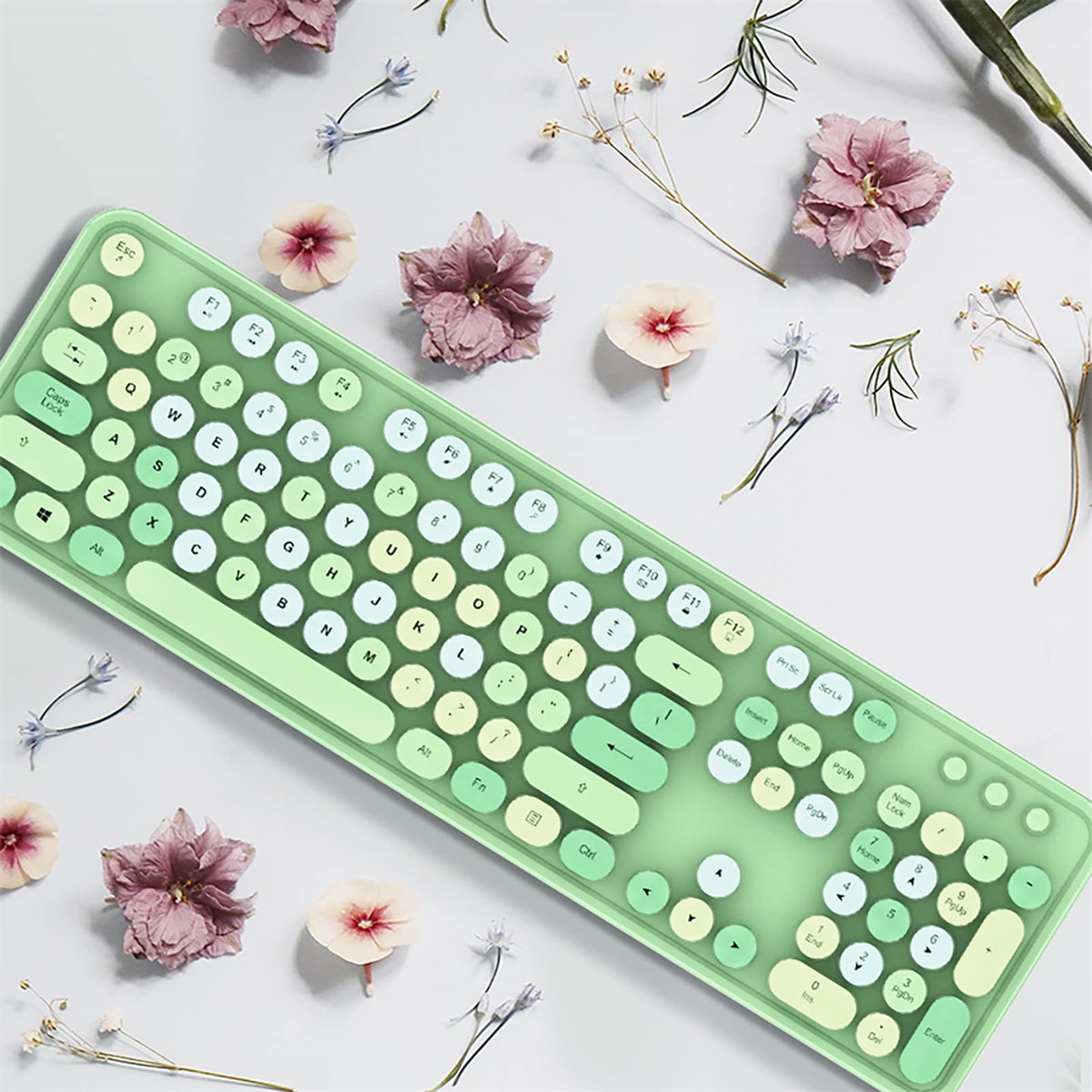 Grüne kabellose Tastatur mit weißen Tasten und Blumen auf weißer Oberfläche.