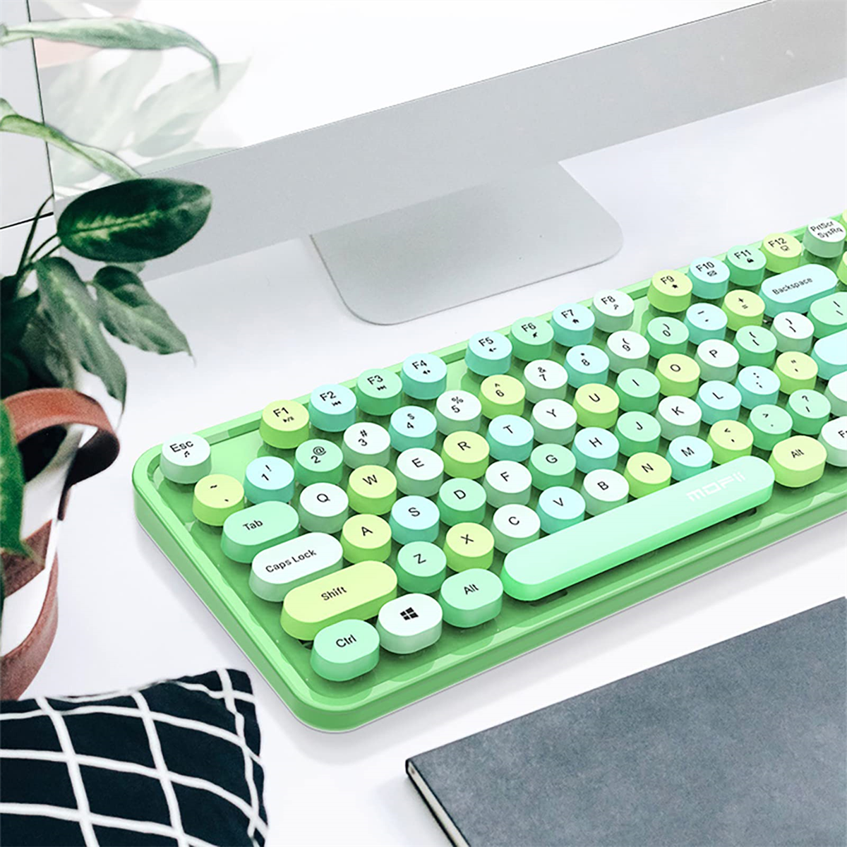 Grüne Retro-Tastatur mit runden Tasten, ein weißer Monitor und eine Topfpflanze auf dem Schreibtisch.