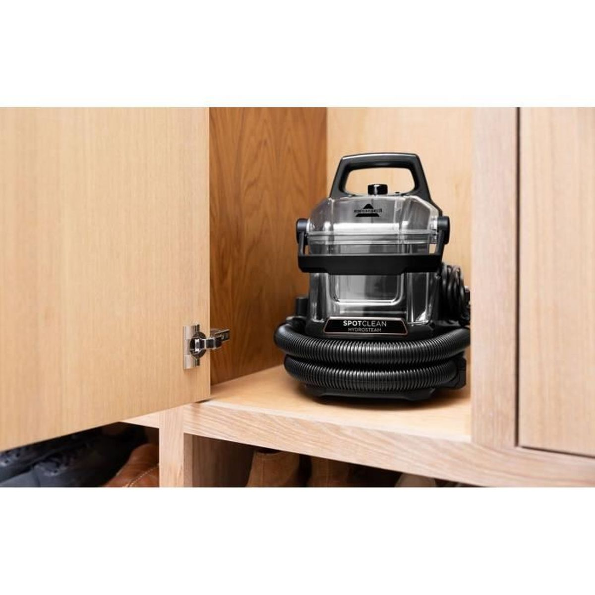 Bissell SpotClean ProHeat Staubsauger in einem Holzschrank mit schwarzem Schlauch.