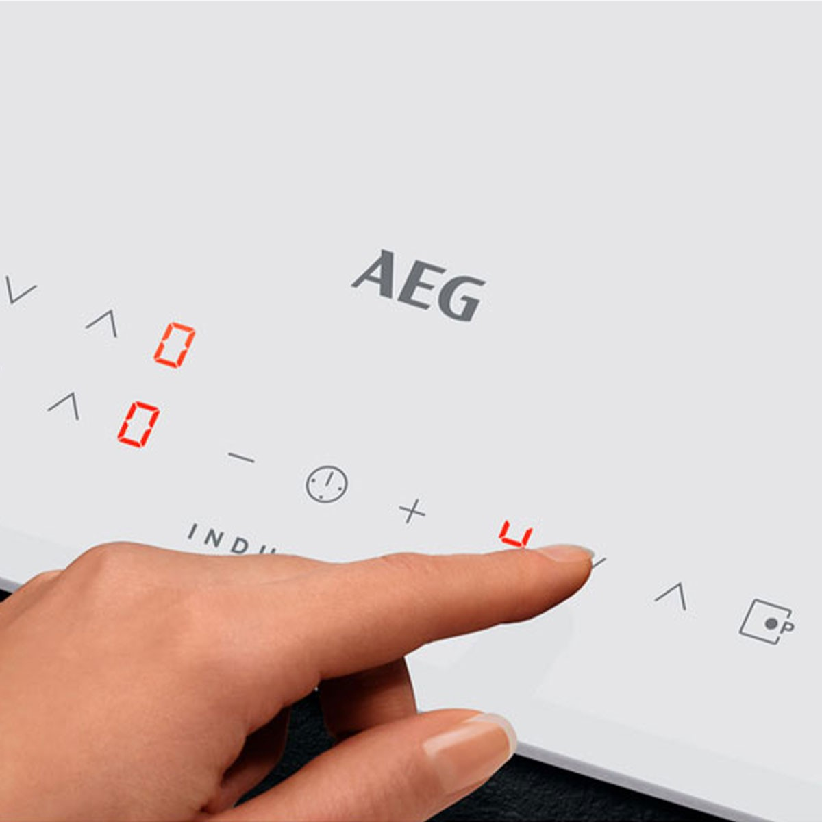 Una mano tocca un piano cottura a induzione. AEG è in alto, numeri e simboli sono visibili.