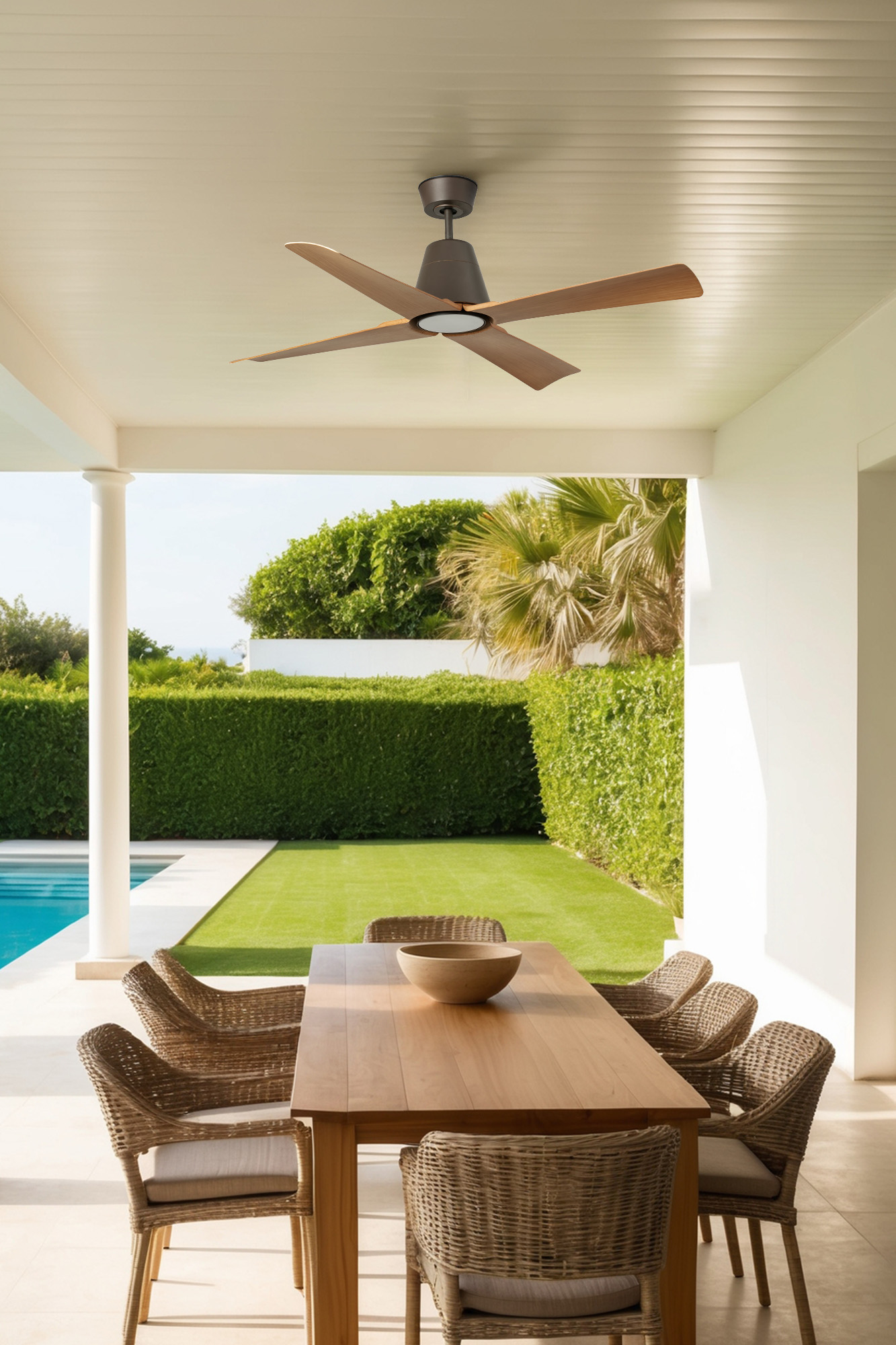 Patio all'aperto con ventilatore a soffitto, tavolo, sedie, piscina e siepe verde sullo sfondo.