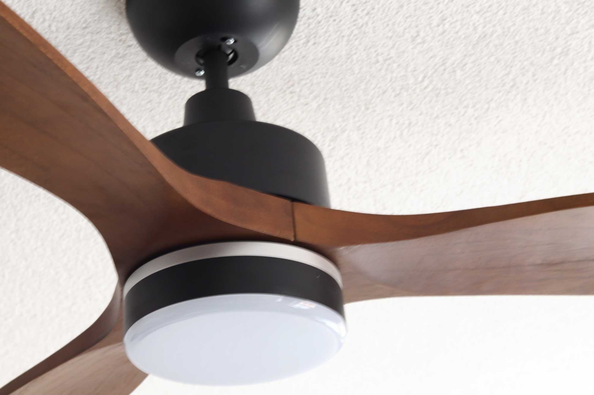 Nahaufnahme eines Deckenventilators mit Holzflügeln, einem schwarzen Motorgehäuse und einem weißen Licht.