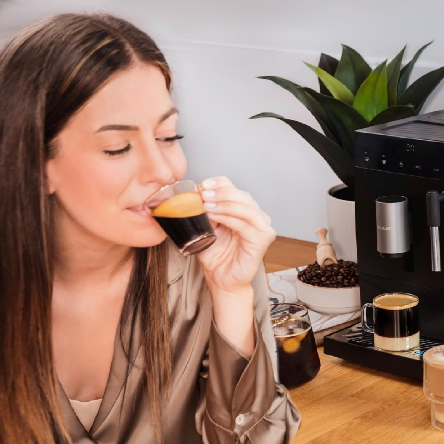 Una donna beve caffè da un bicchiere davanti a una macchina da caffè con chicchi di caffè.