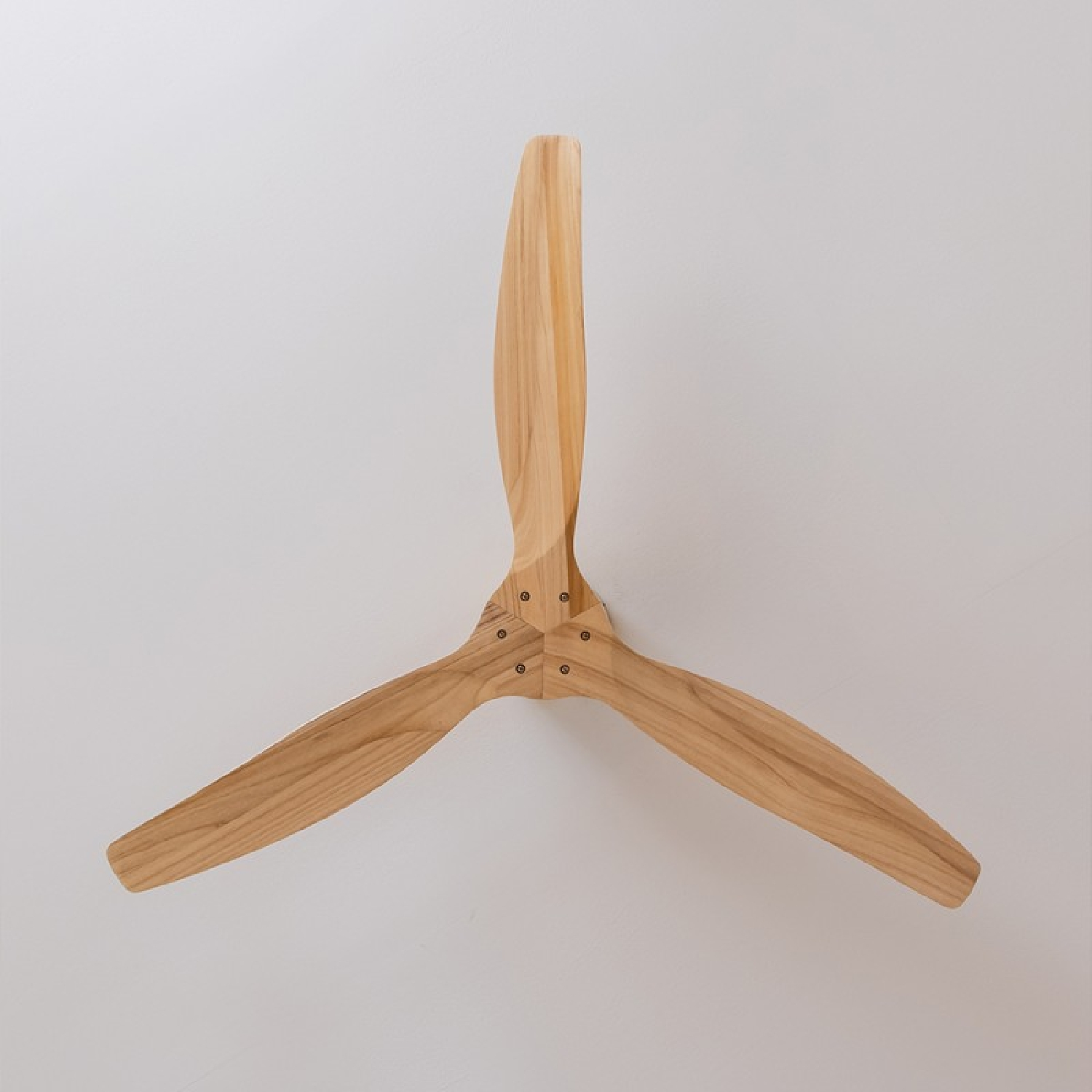 Holzdeckenventilator mit drei Blättern. Er ist an einer weißen Wand montiert.