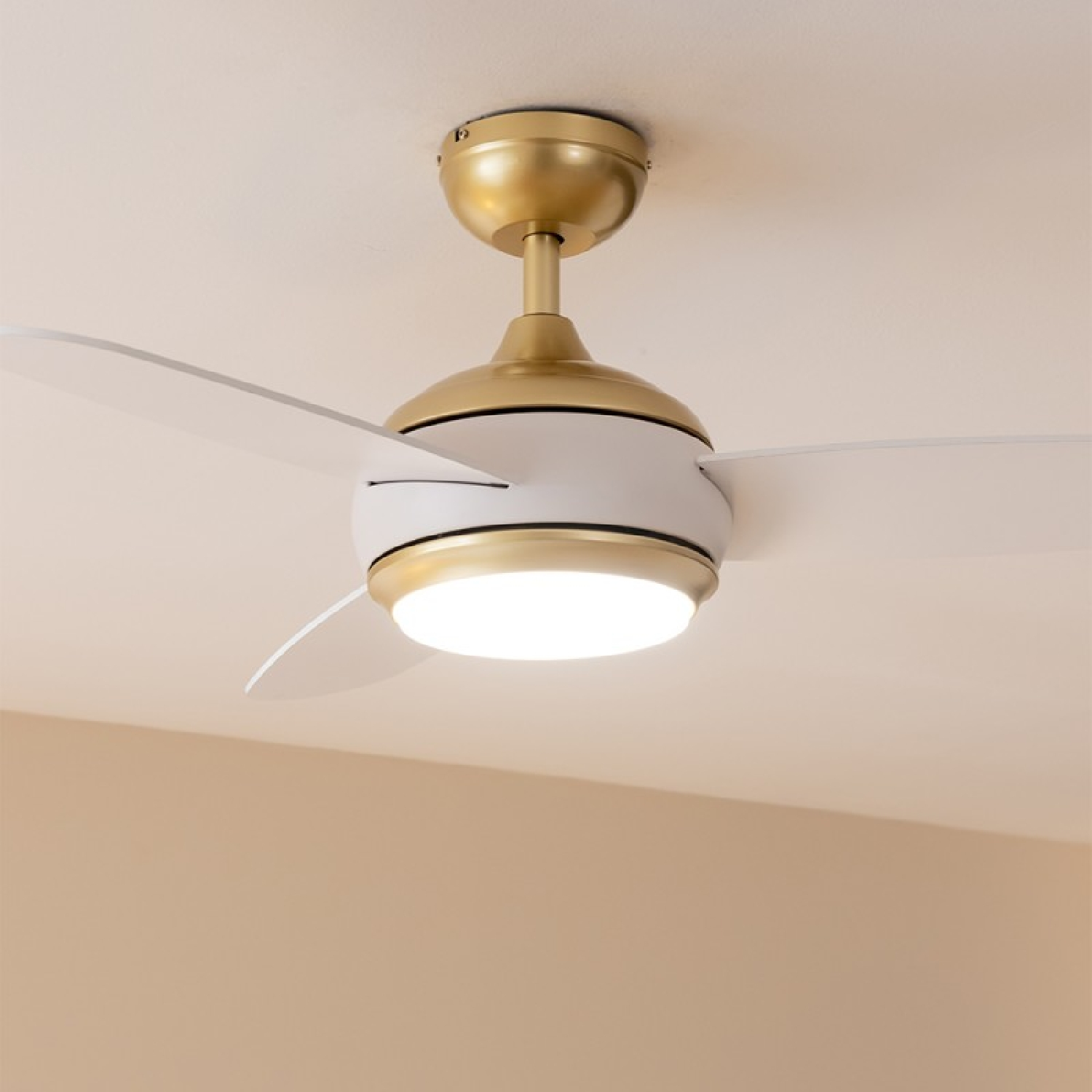 Ventilatore a soffitto con luce. Finitura oro e bianca. Pale bianche, dettagli dorati e un apparecchio.