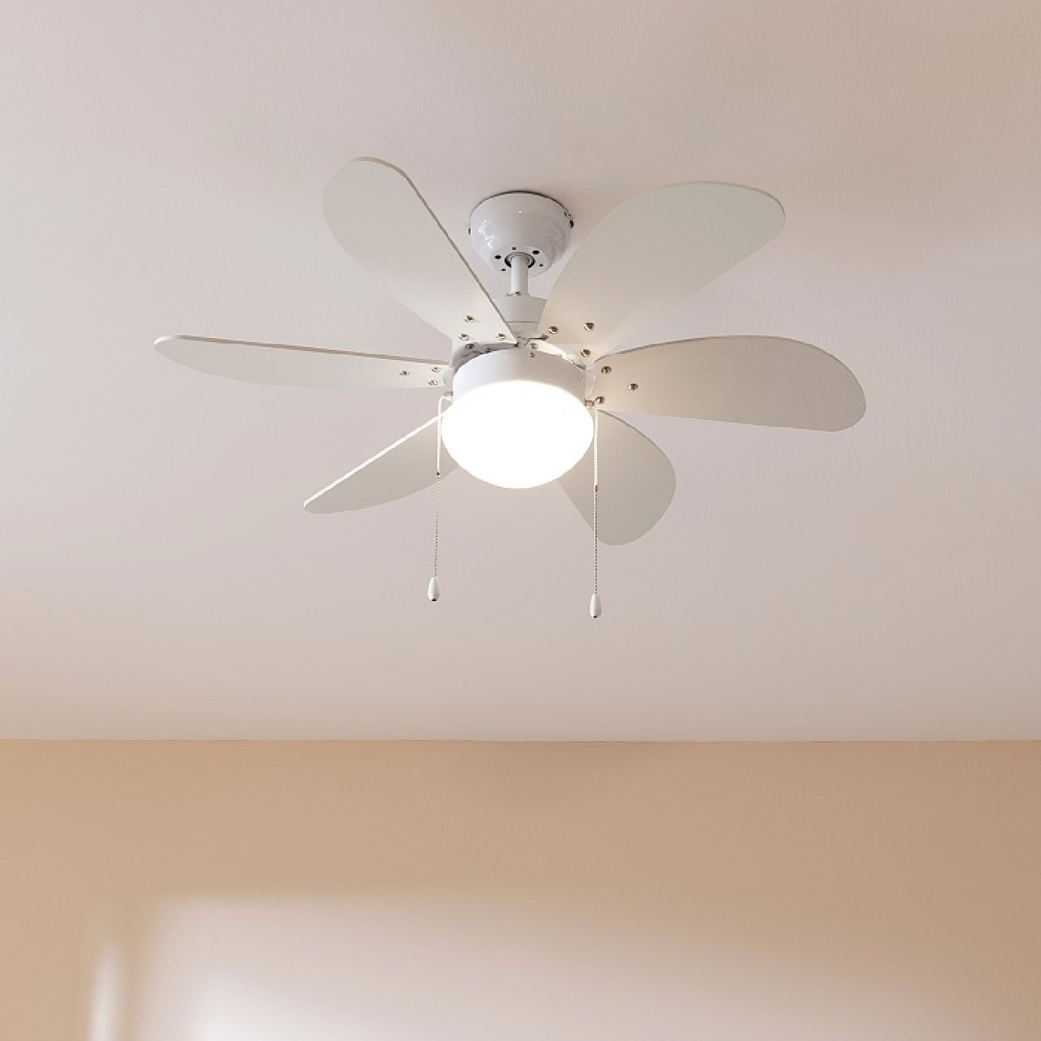 Weißer Deckenventilator mit fünf Flügeln und zentraler Leuchte. Beigefarbene Decke.