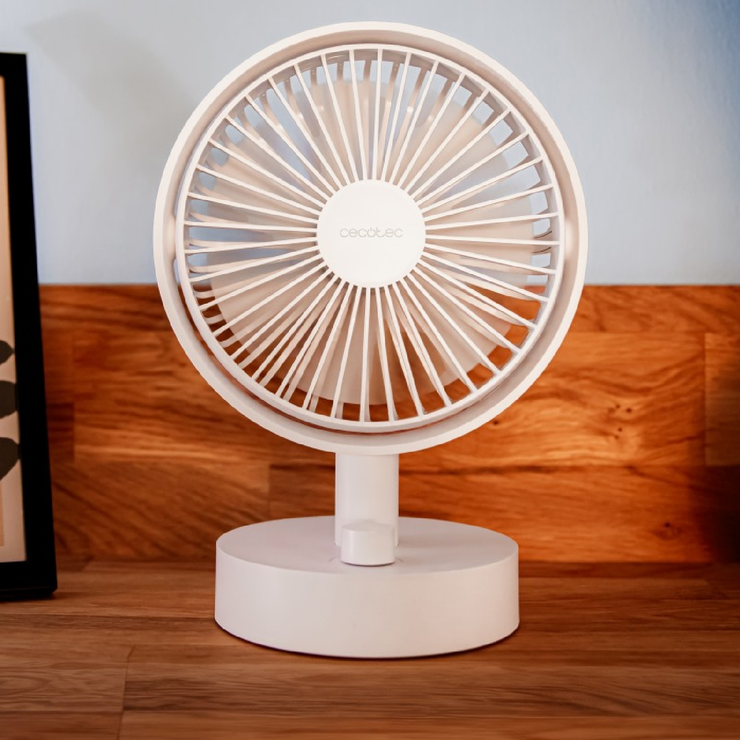 Piccolo ventilatore da scrivania bianco su una superficie di legno. La ventola è accesa.