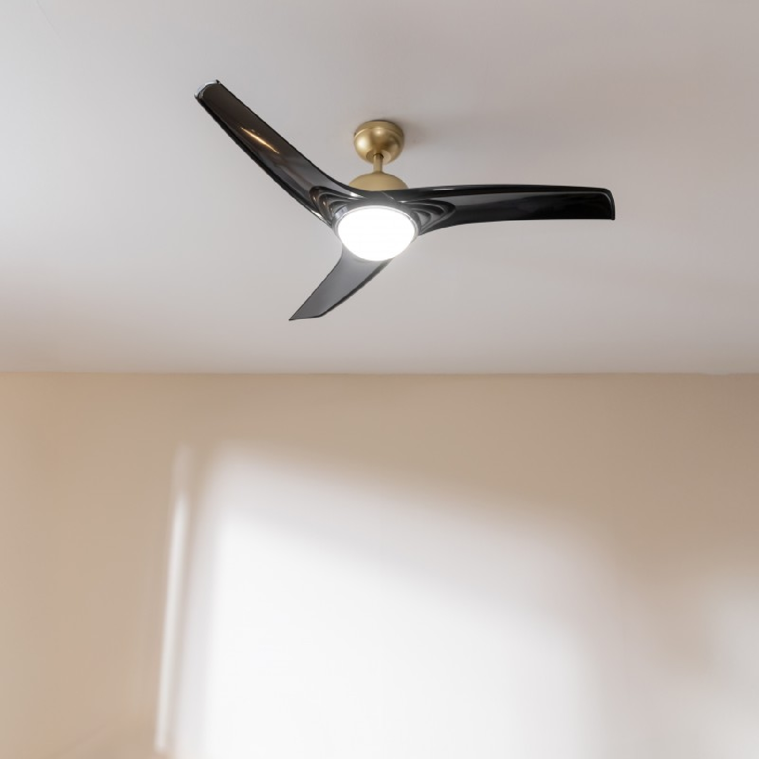 Un ventilatore da soffitto nero con tre pale e una luce centrale, accento oro.