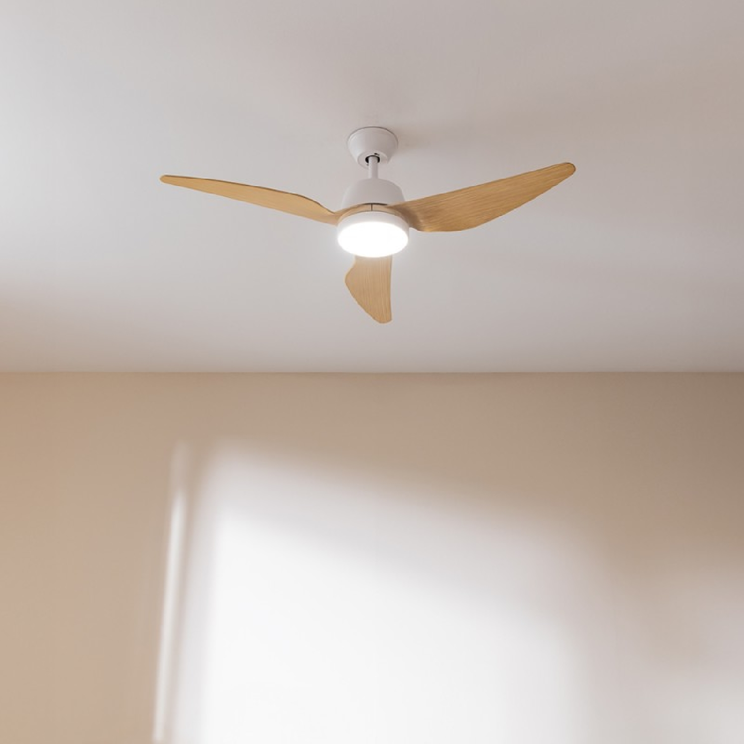 Ein Deckenventilator mit Holzflügeln und einer zentralen Leuchte, montiert an einer weißen Decke.