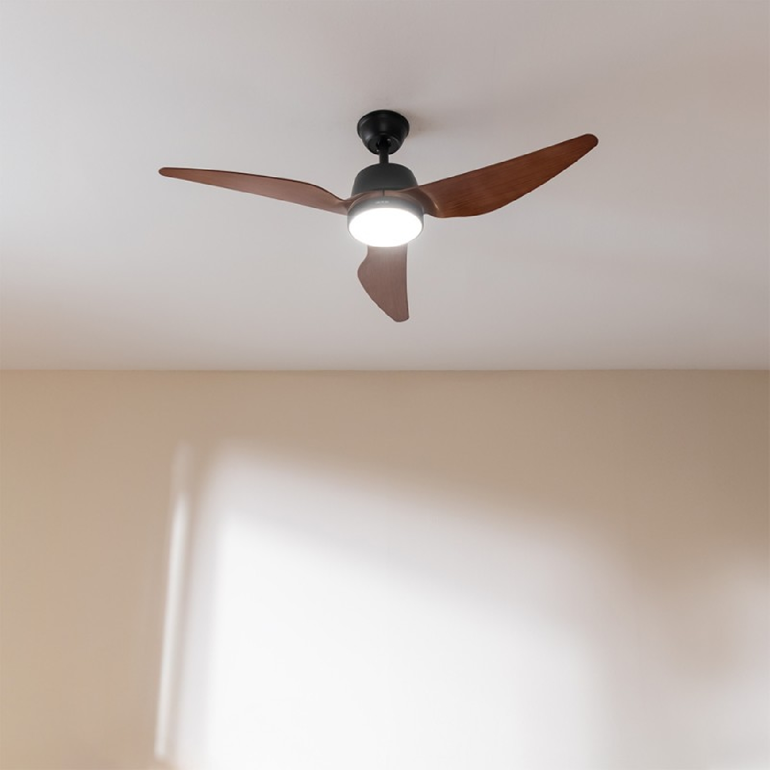 Un ventilador de techo con aspas marrones y un motor negro está montado en un techo blanco.