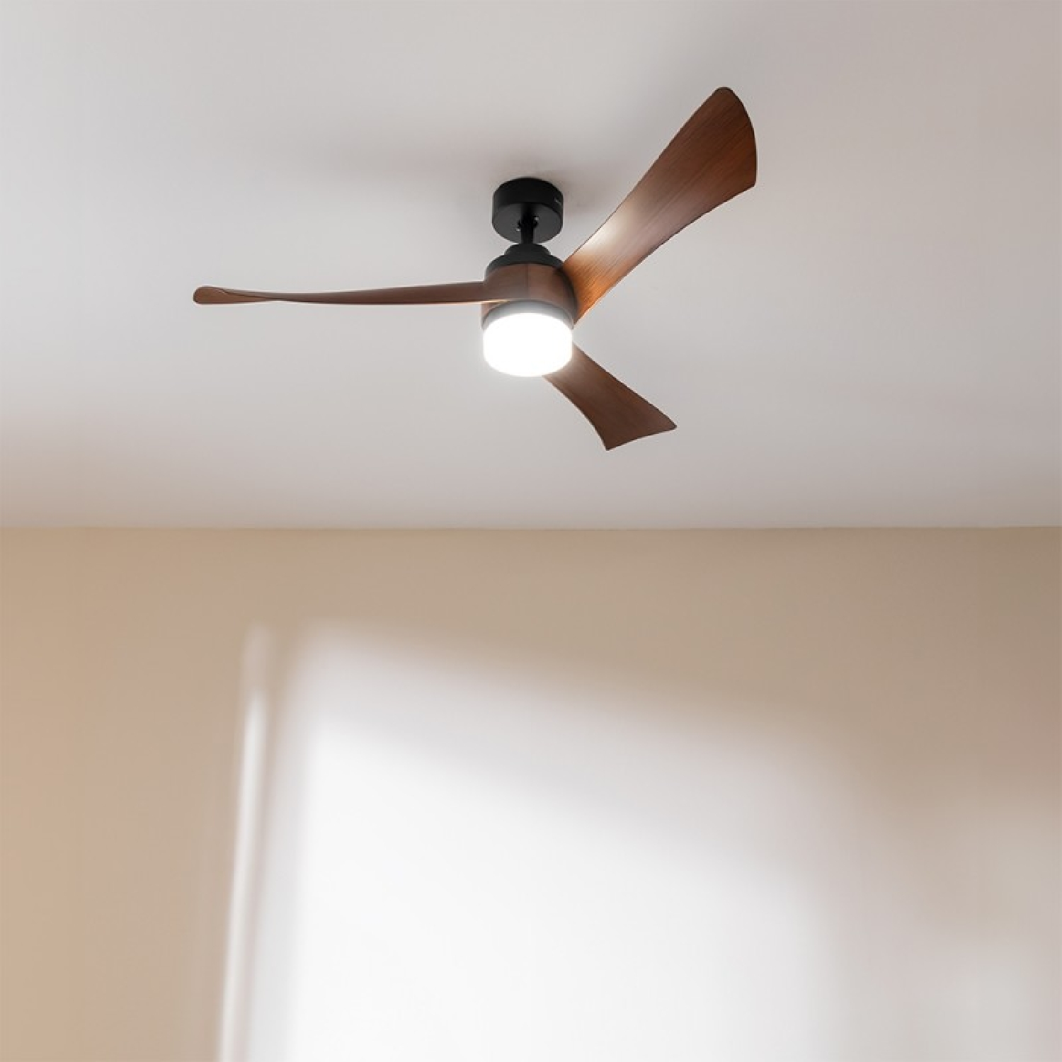 Deckenventilator mit Holzflügeln und Licht. Der Ventilator ist an einer weißen Decke befestigt.