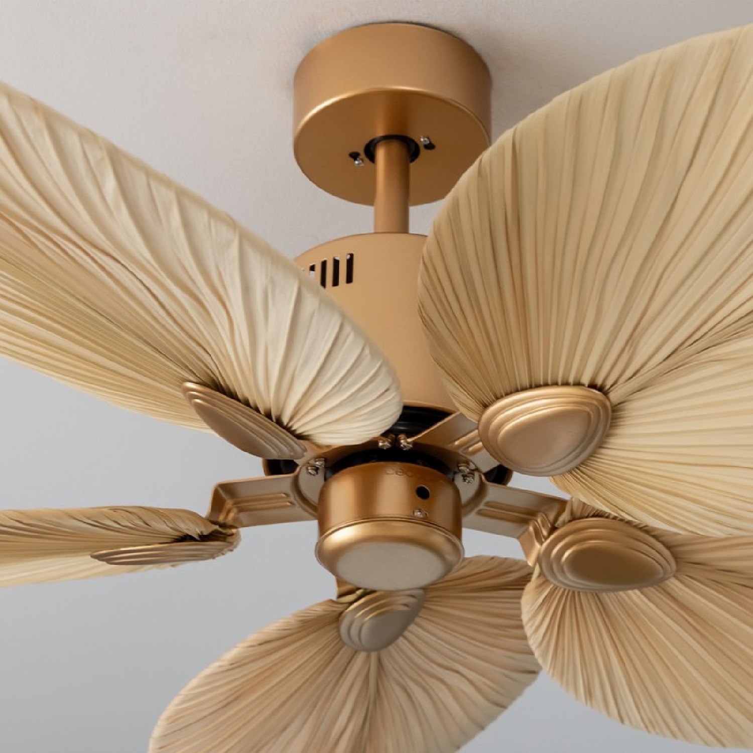 Ventilador de techo dorado con aspas beige. Vista de cerca desde abajo.