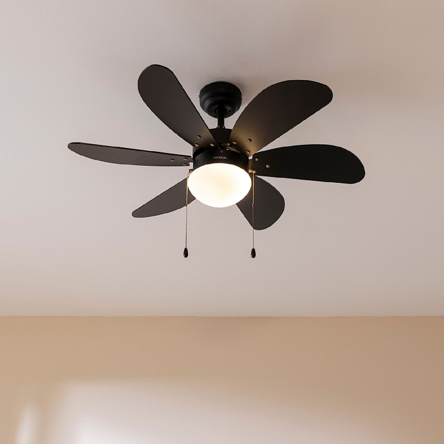Un ventilatore da soffitto nero con sei pale e una luce centrale. È montato su un soffitto bianco.