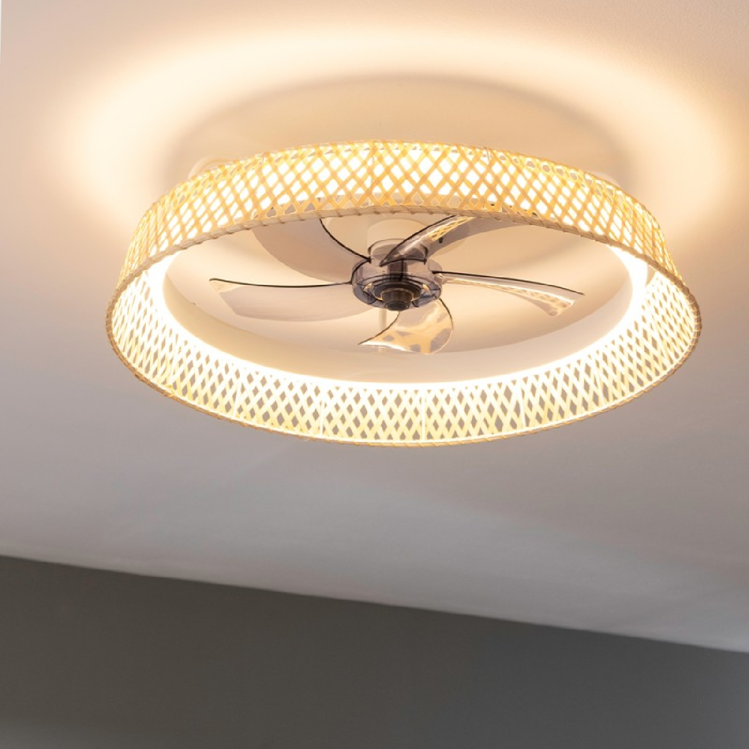 Ventilador de techo con pantalla tejida y luz, con techo claro y techo oscuro en el fondo.
