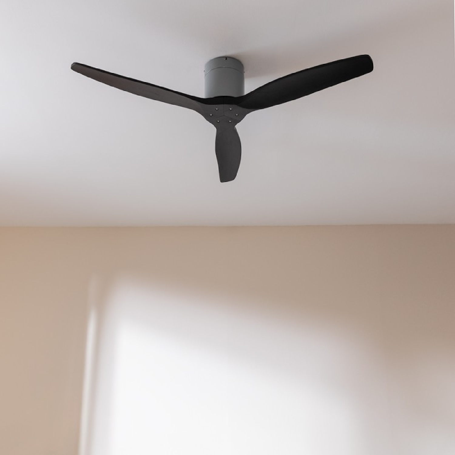 Deckenventilator mit drei schwarzen Flügeln vor einer beigen Wand und weißer Decke.