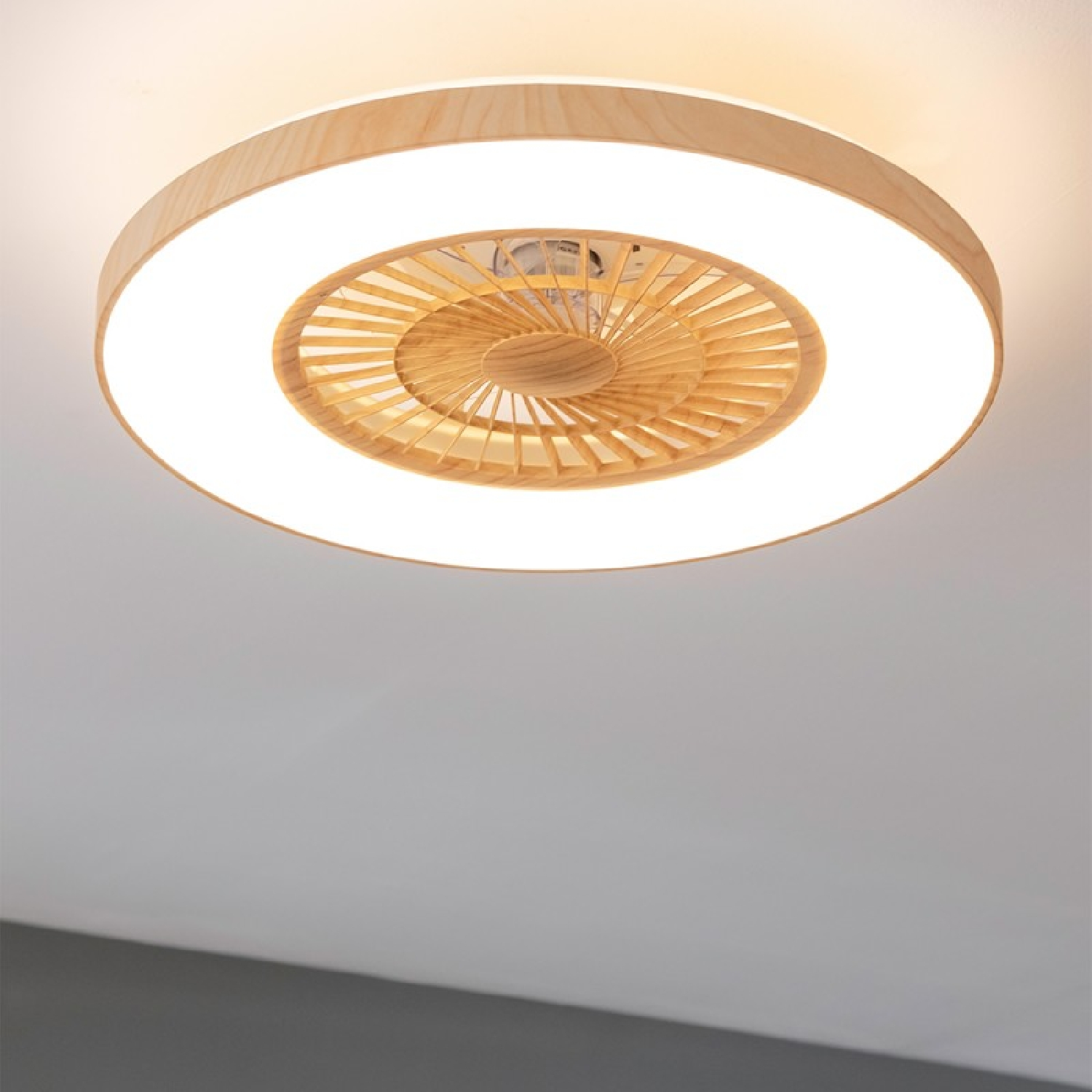 Un ventilador de techo de madera con luz circular. Está montado en un techo blanco, creando una iluminación suave.