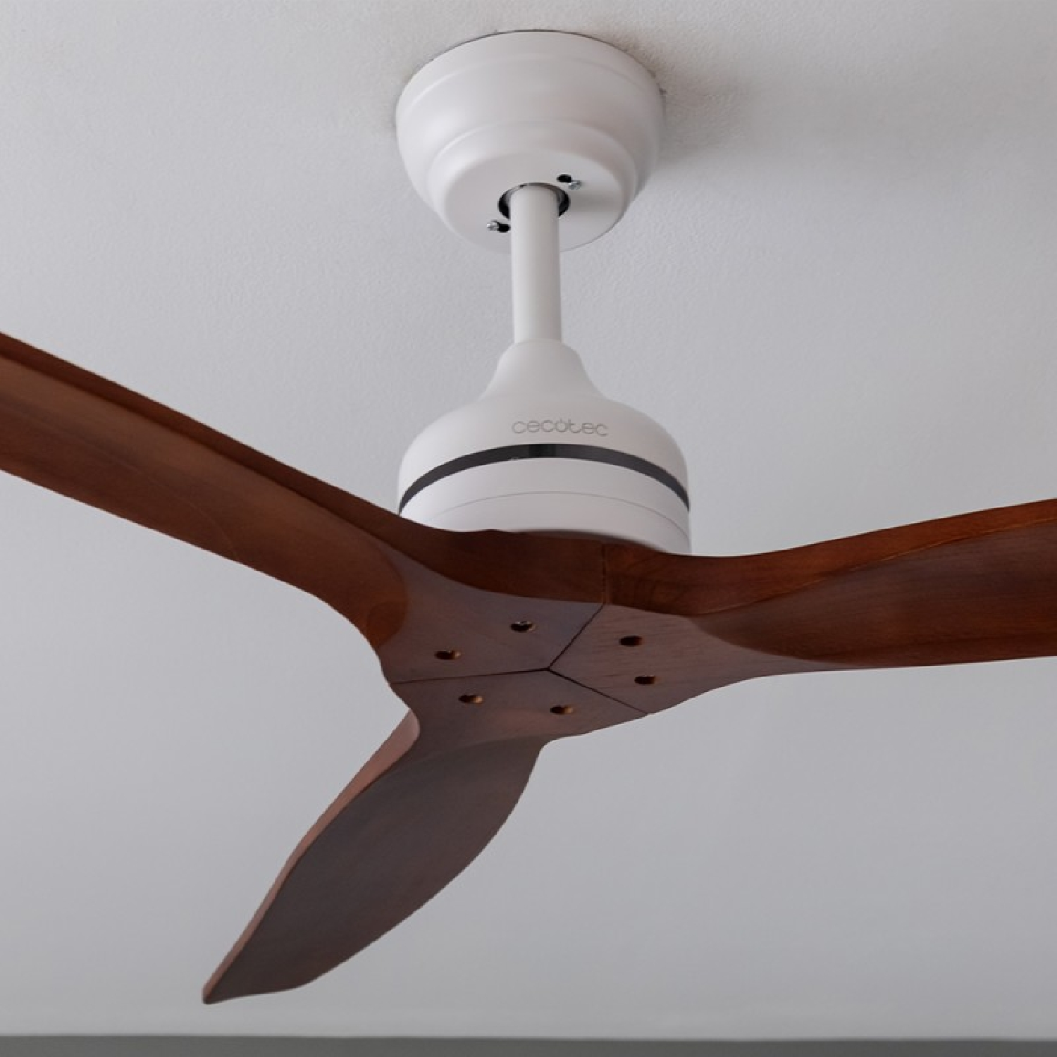 Ventilatore a soffitto con tre pale in legno, carter motore bianco, su un soffitto bianco.