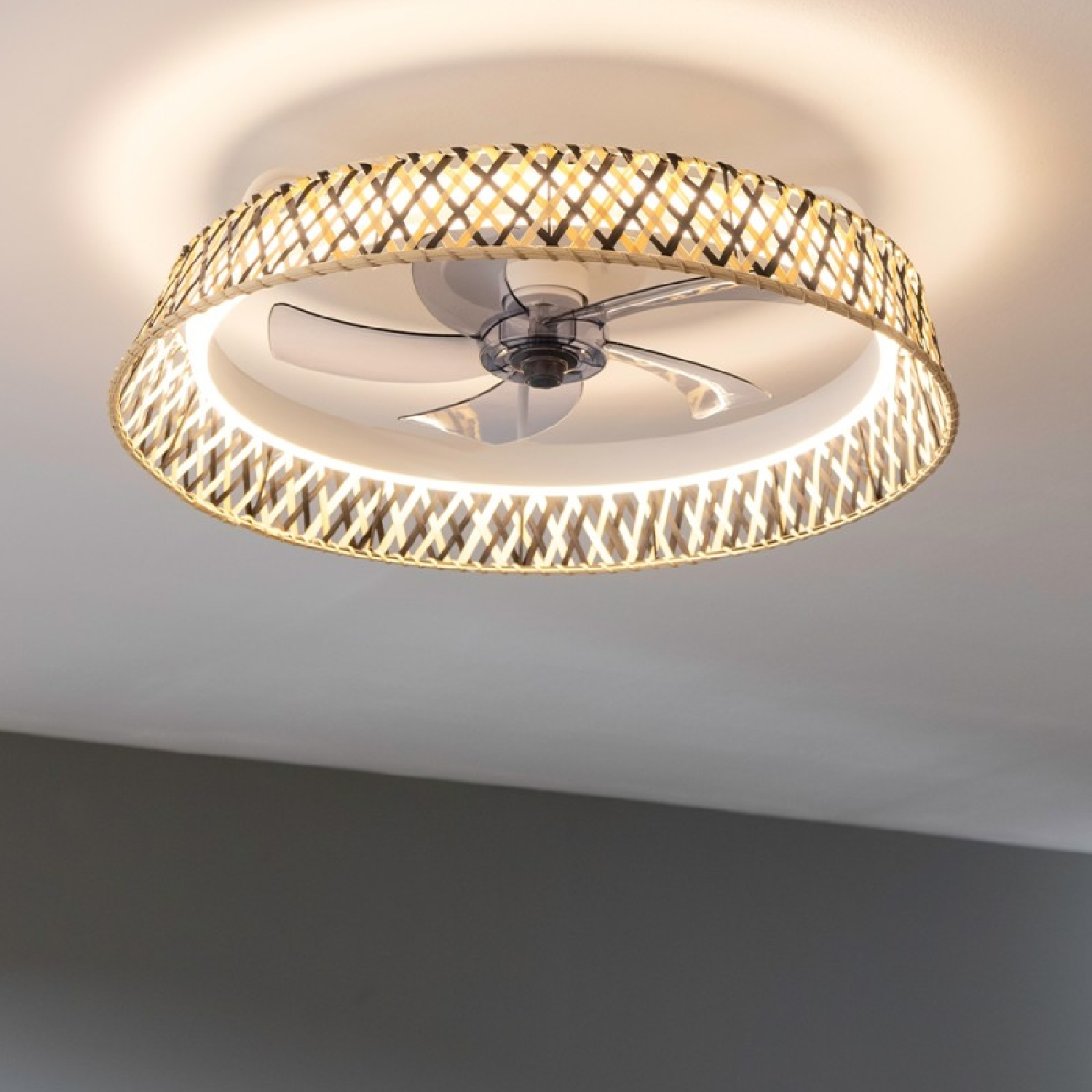 Un ventilador de techo con una pantalla de estilo mimbre. El ventilador es plateado con un anillo de luz alrededor.