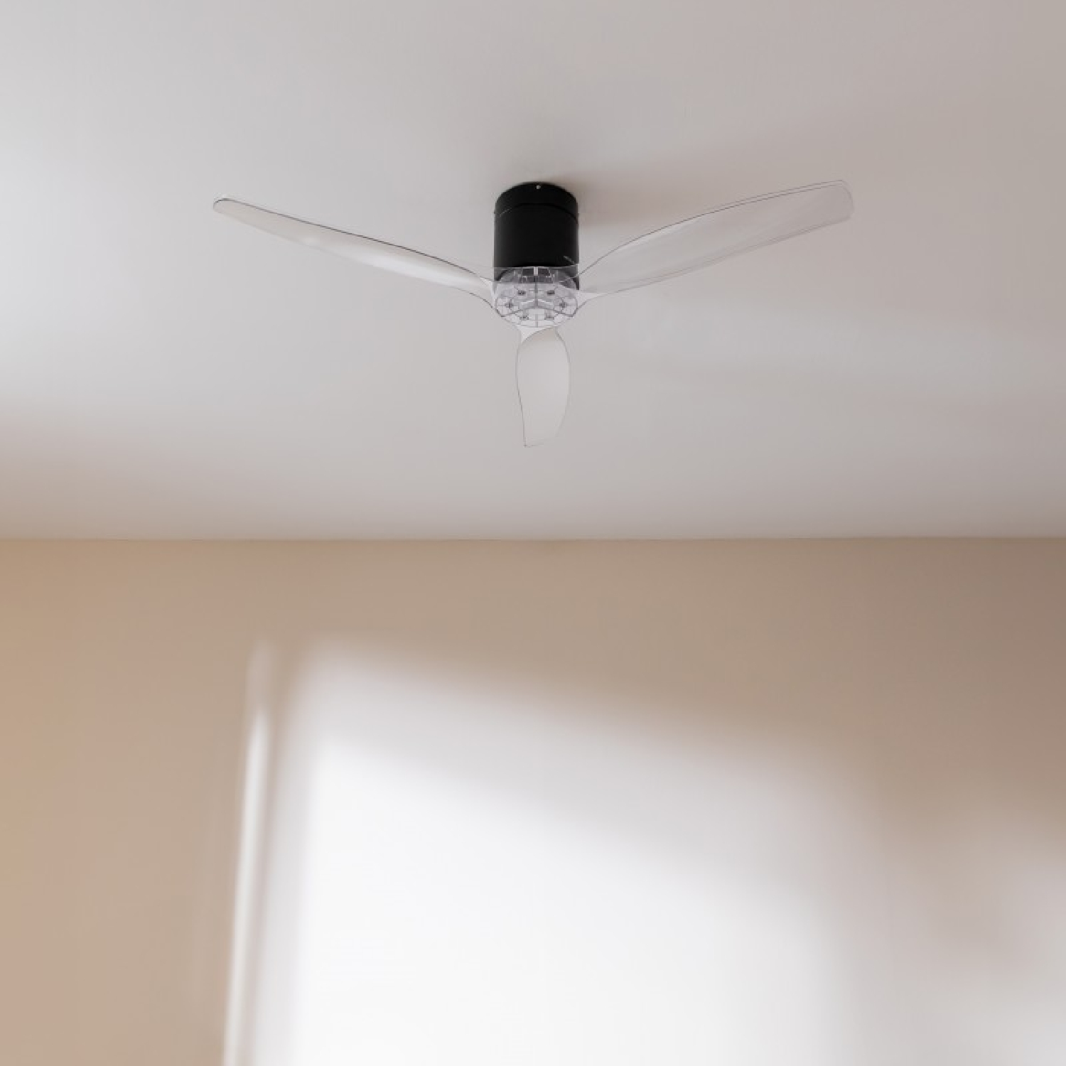 Ventilatore da soffitto con pale trasparenti, montato su soffitto bianco, spento.