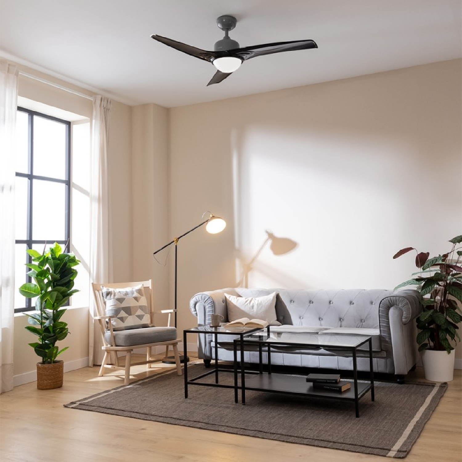 Salón con sofá gris, silla de madera, mesa de centro y ventilador de techo. Ventana y plantas.