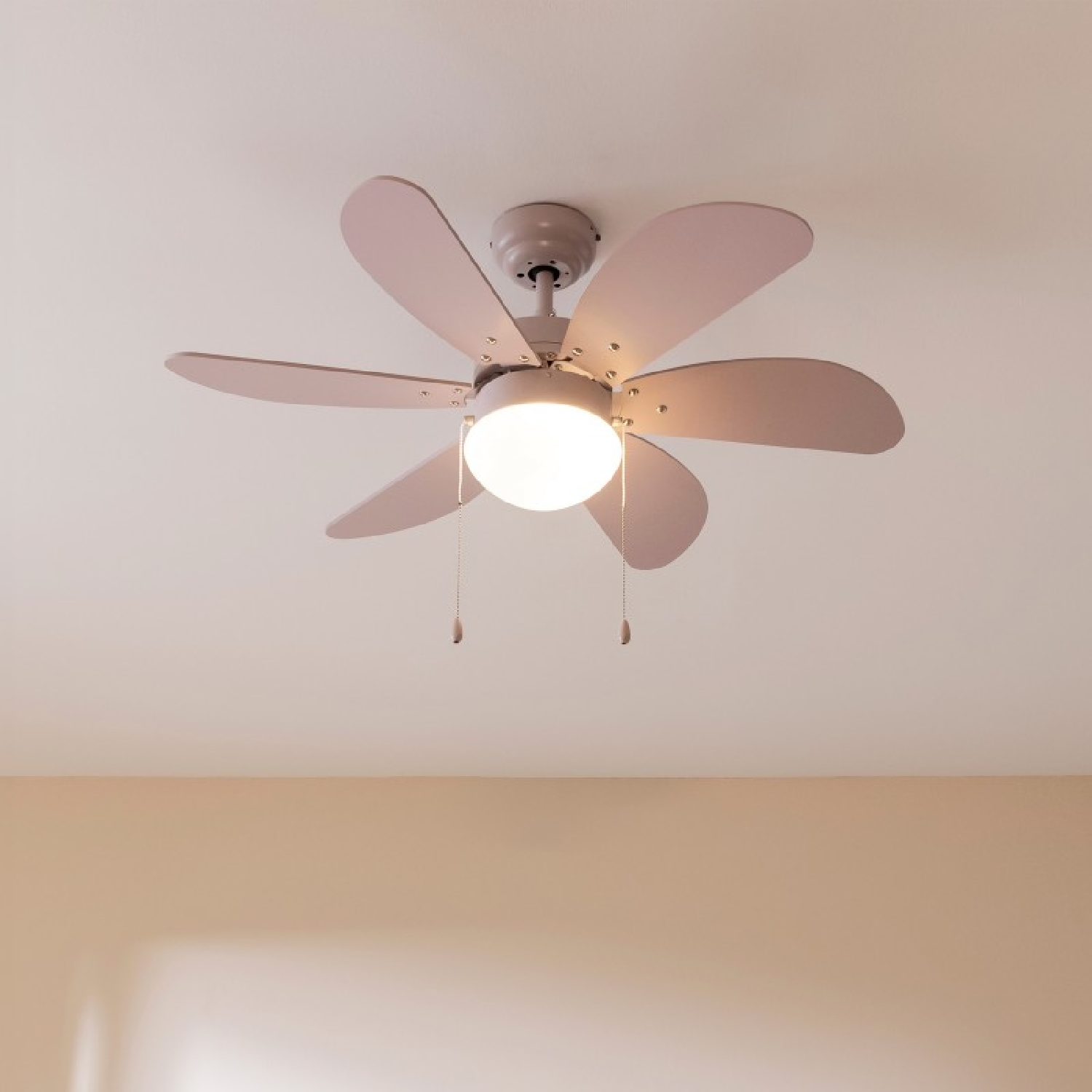 Ein Deckenventilator mit sechs rosa Flügeln und einem zentralen Licht, vor einer weißen Decke.