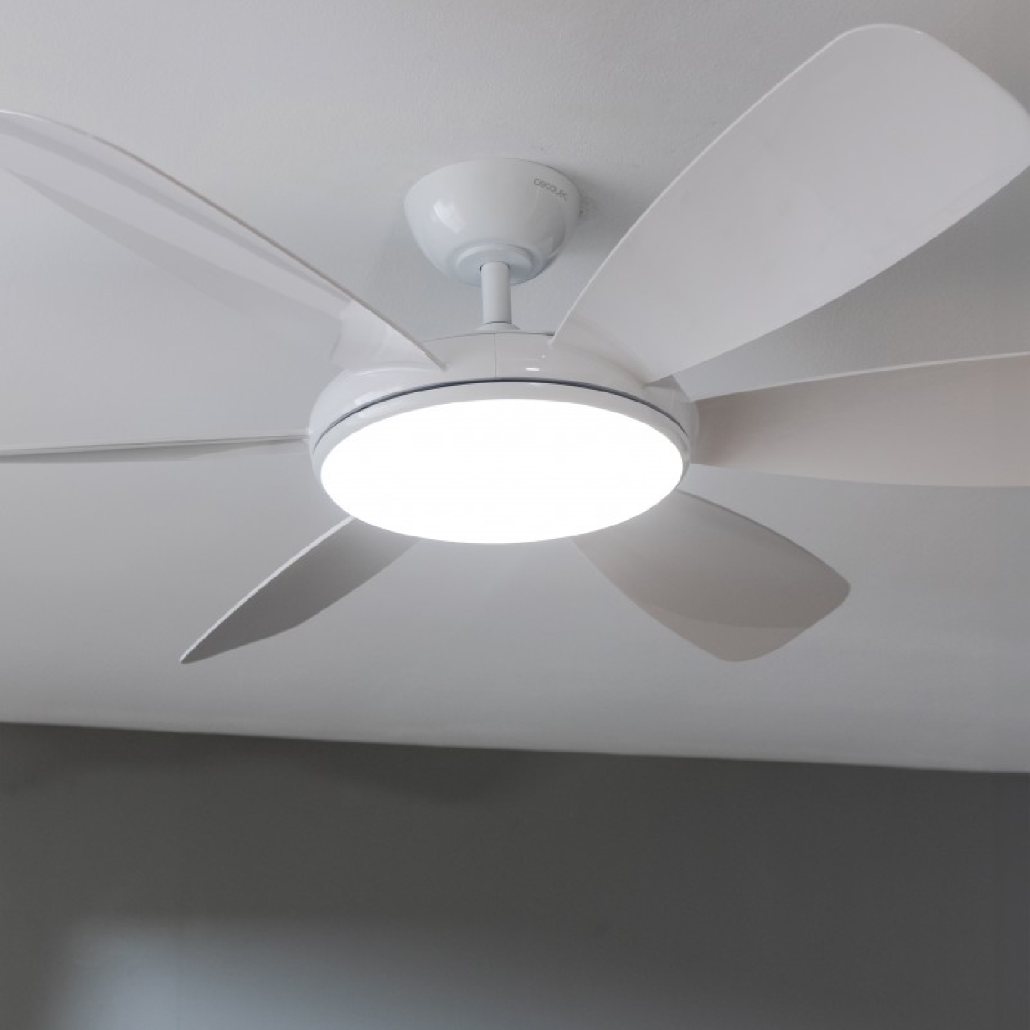 Ventilador de techo blanco con cinco aspas y una luz central, montado en un techo blanco.