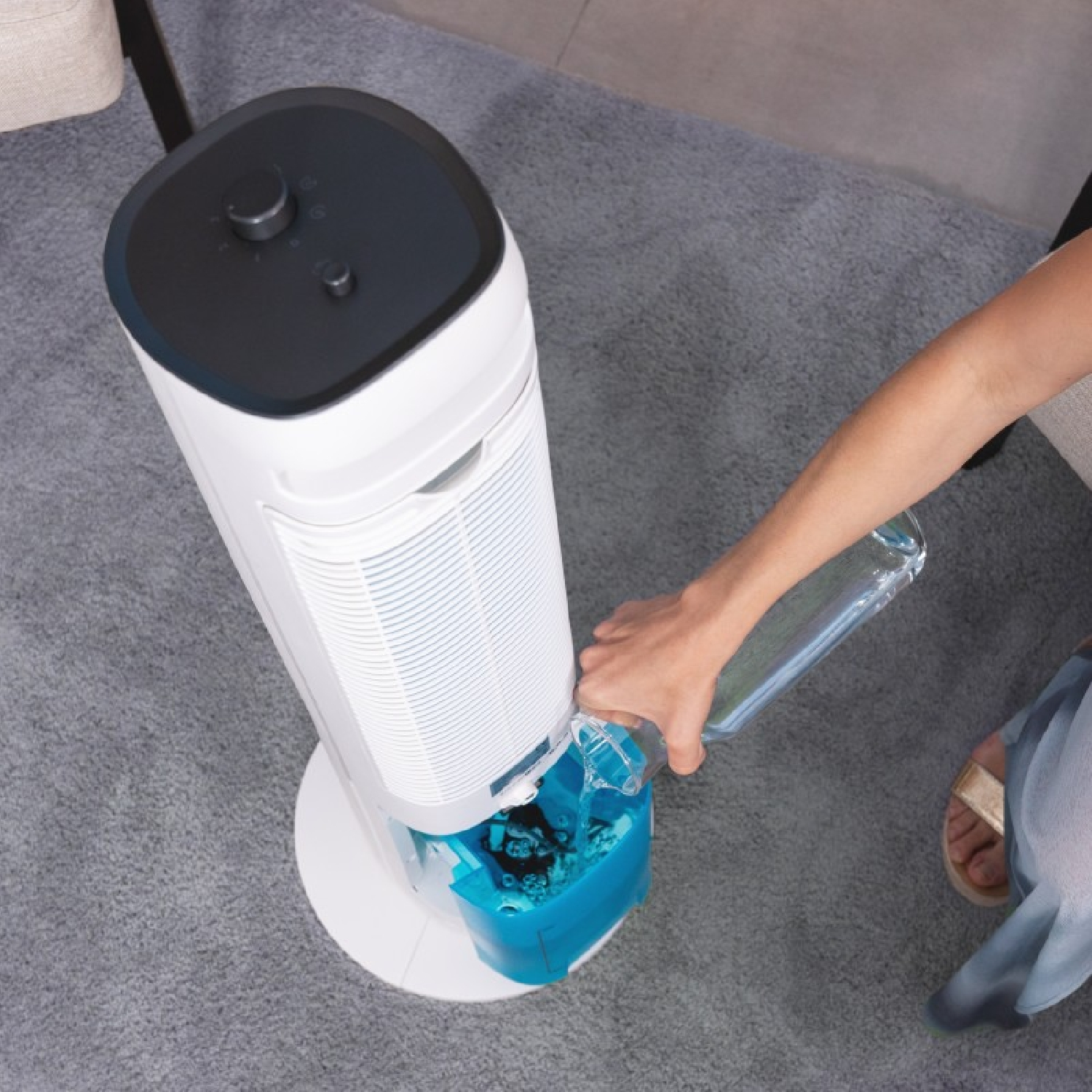 Una persona versa acqua in un umidificatore bianco e blu con una bottiglia d'acqua trasparente.