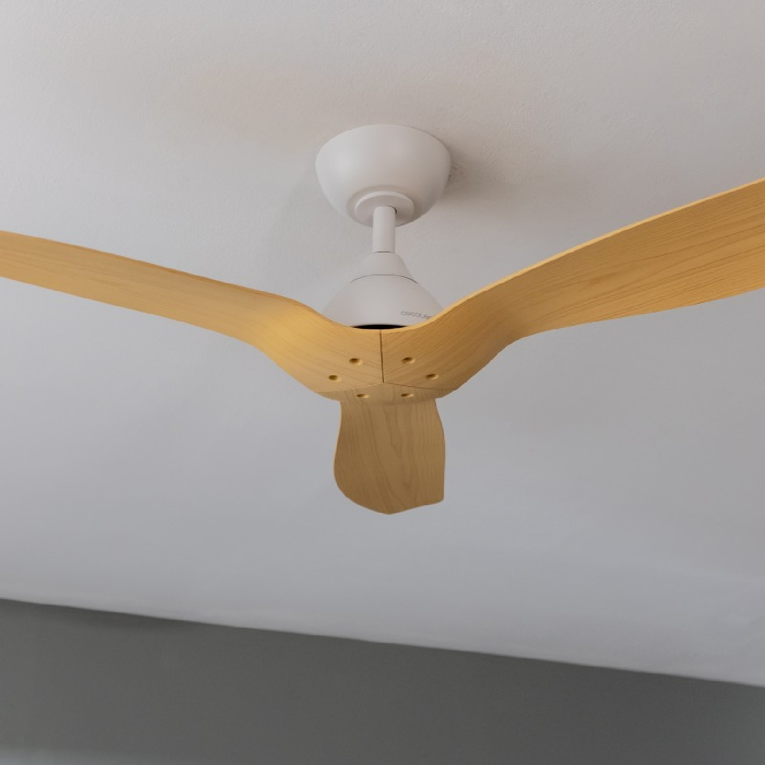 Ventilatore a soffitto con tre pale in legno chiaro e un motore bianco. Il soffitto è bianco.