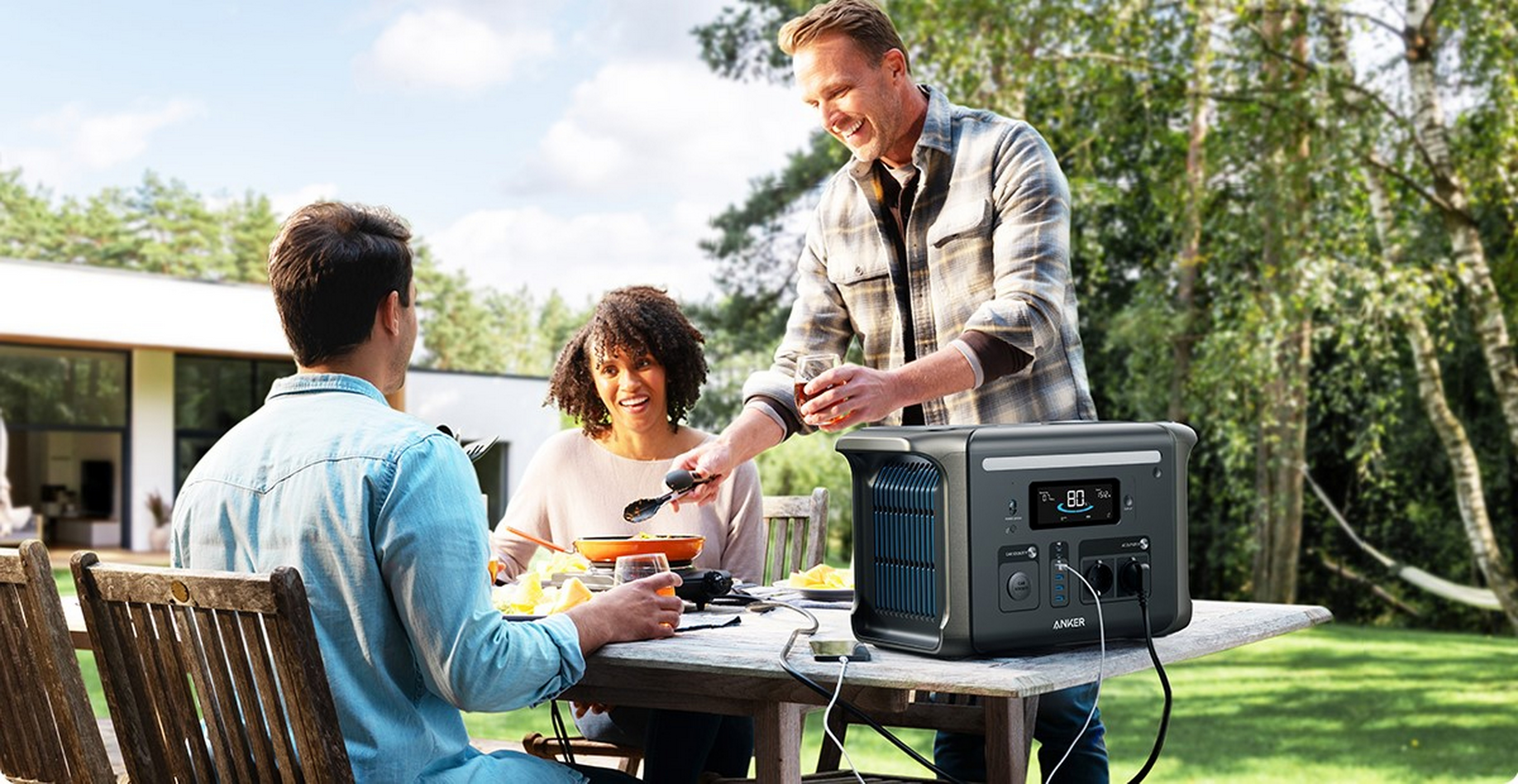 Trzy osoby wokół stołu na zewnątrz, ze stacją zasilania i akcesoriami.