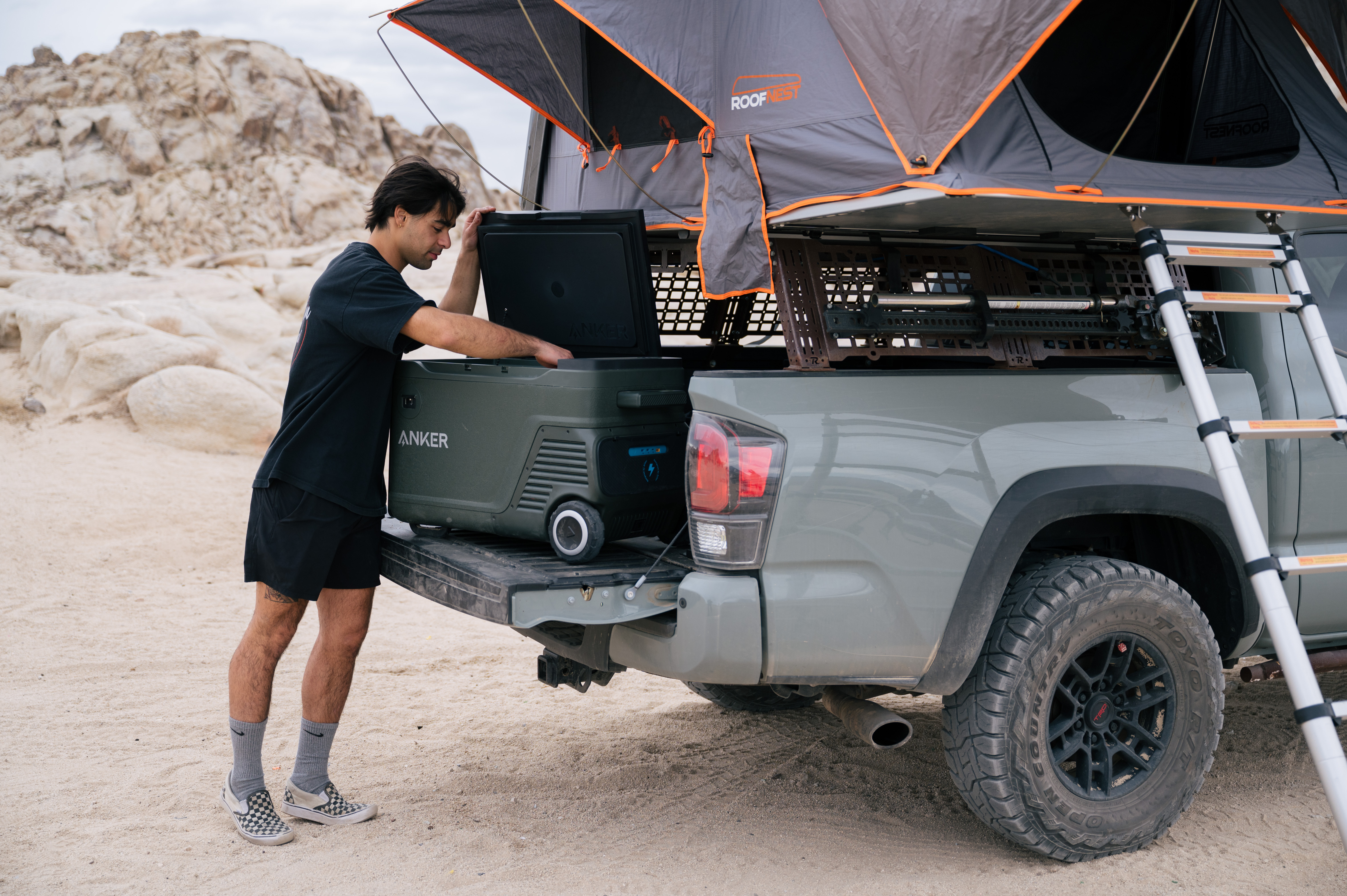Mężczyzna otwiera chłodziarkę z tyłu ciężarówki z namiotem na górze, w scenerii pustynnej.