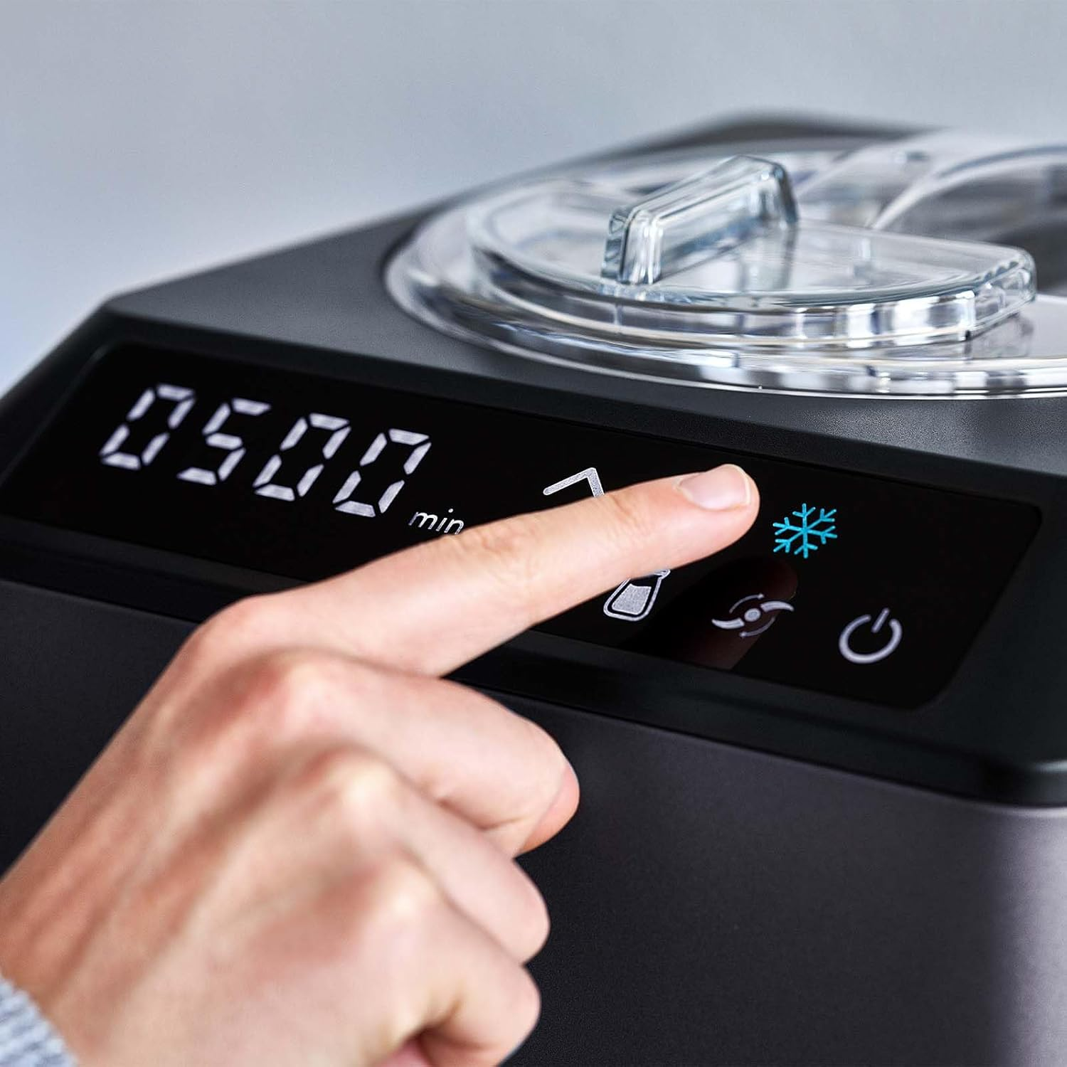 Der Finger einer Person drückt auf ein Schneeflocken-Symbol auf einem schwarzen Eisbereiter mit digitaler Anzeige.