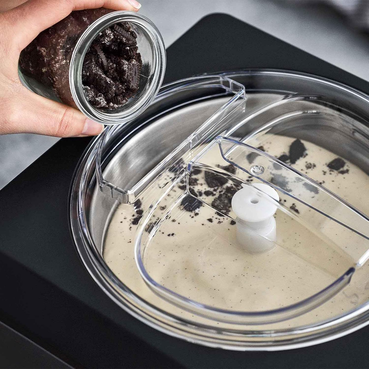 Hand gießt dunkle Krümel in Eismaschine mit cremiger Basis.