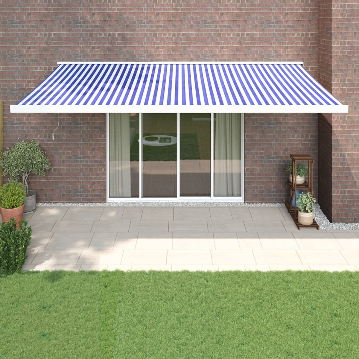 Blau-weiß gestreifte Markise über einer Glasschiebetür, Backsteinmauer, grünes Gras und Terrasse.