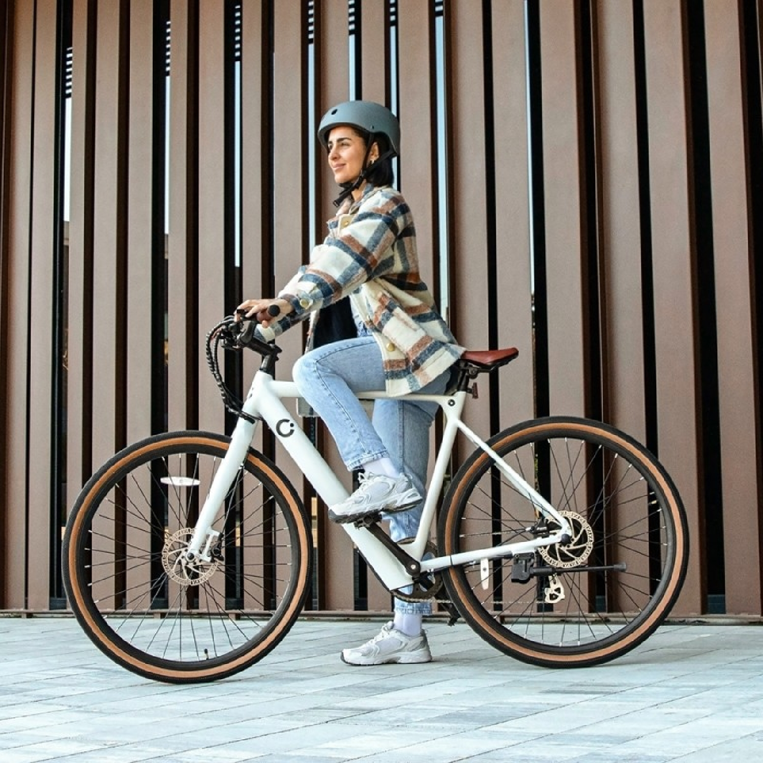 Una mujer monta en bicicleta. Lleva casco y camisa a cuadros, con listones de madera detrás.