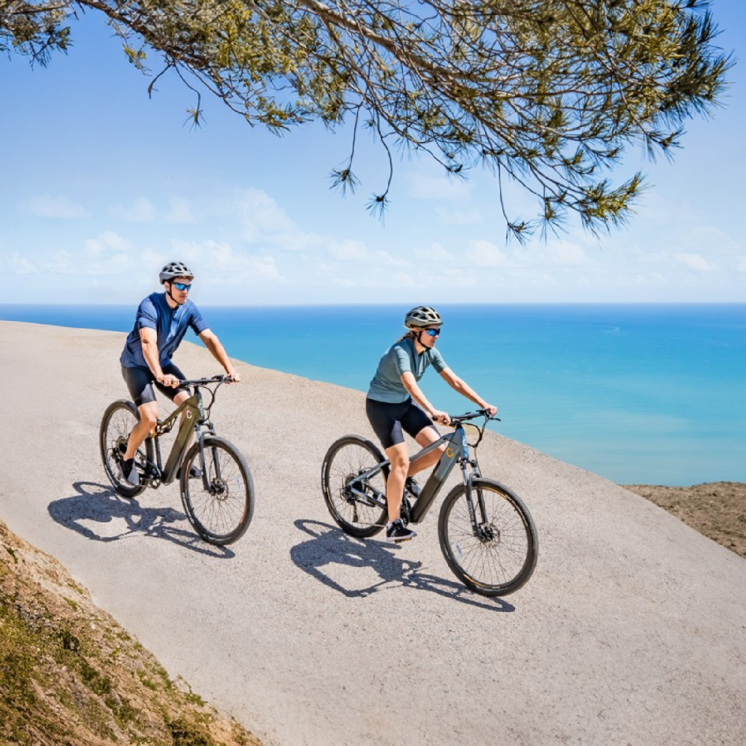 Due ciclisti in bicicletta su una strada asfaltata vicino all'oceano.