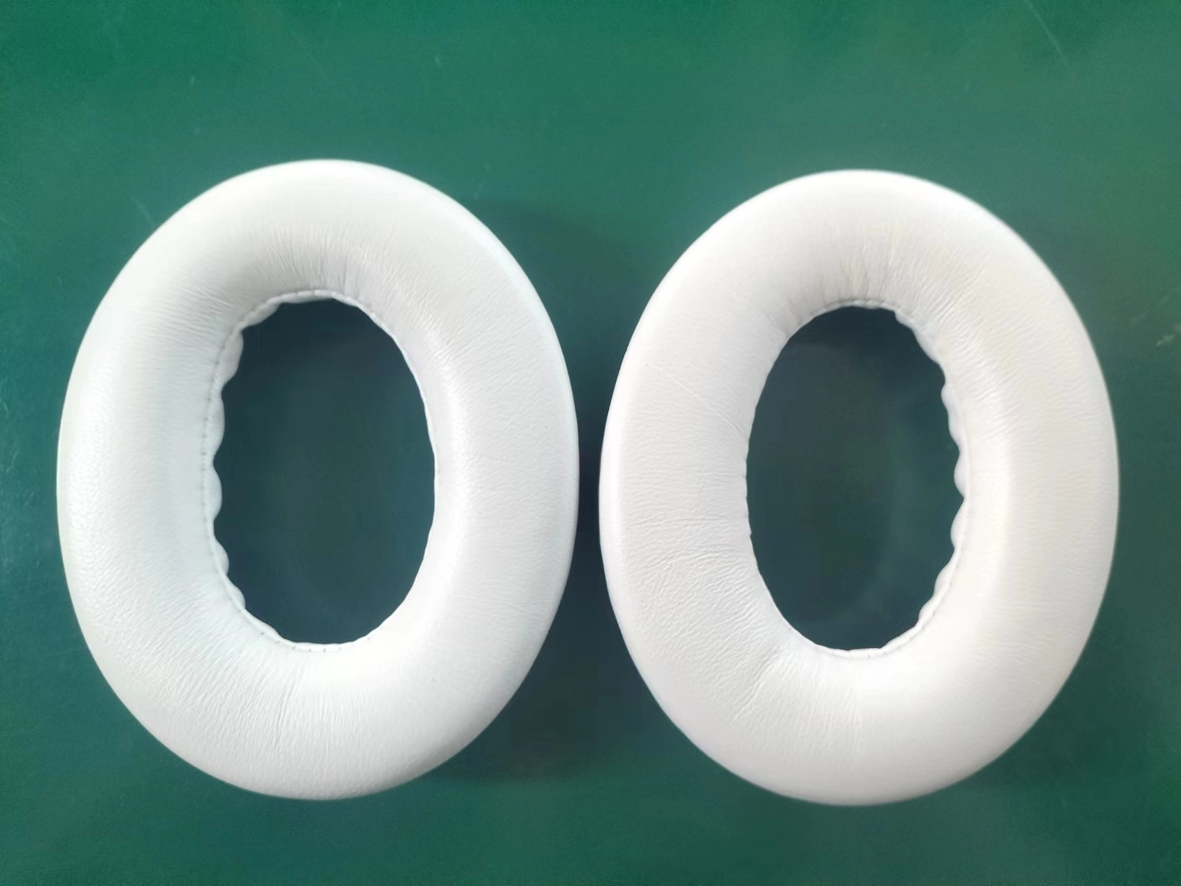 Dwie białe nauszniki, obok siebie, na zielonej powierzchni.