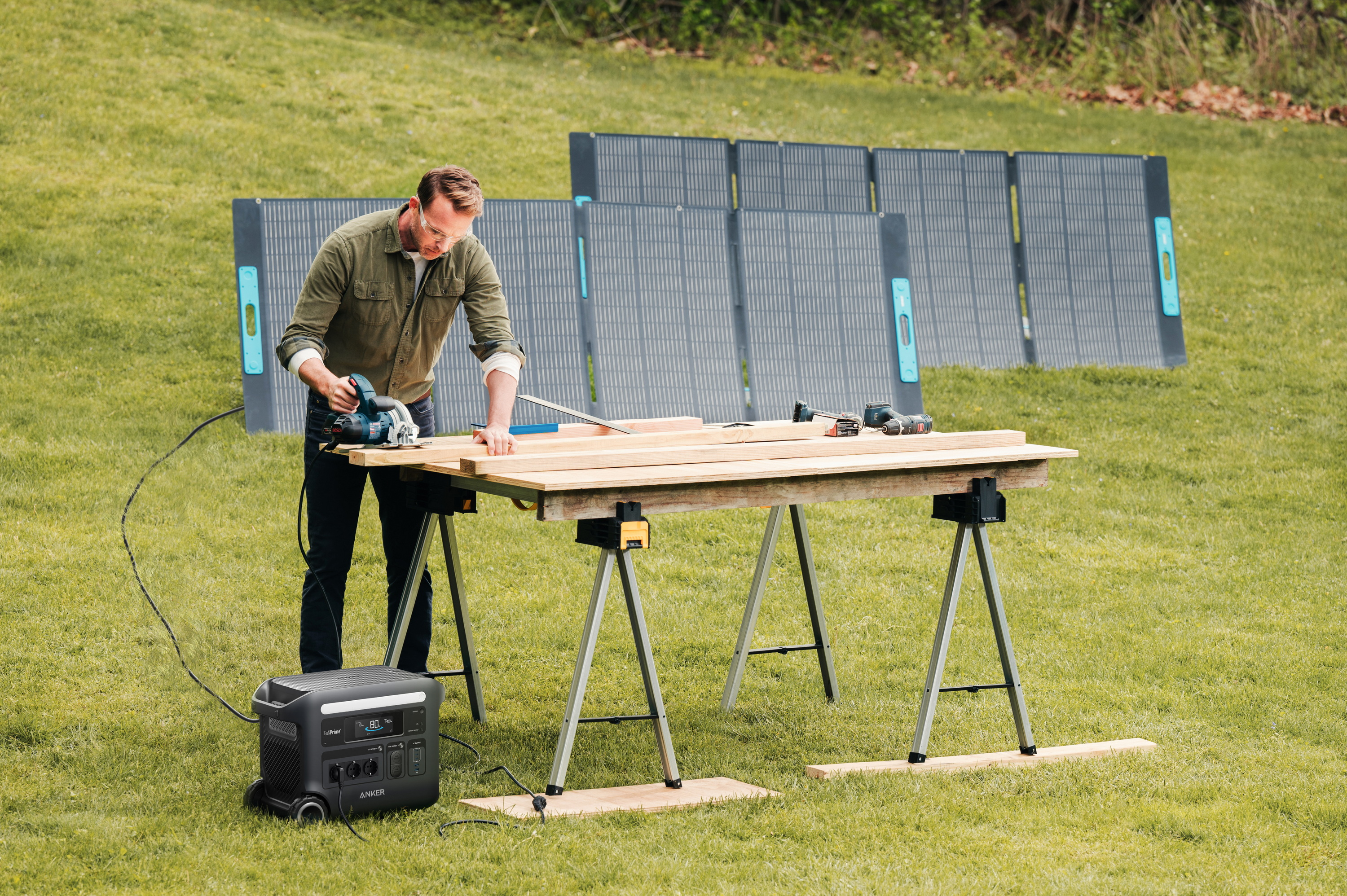 Mężczyzna używający piły do drewna na kozłach z panelami słonecznymi i elektrownią w tle.