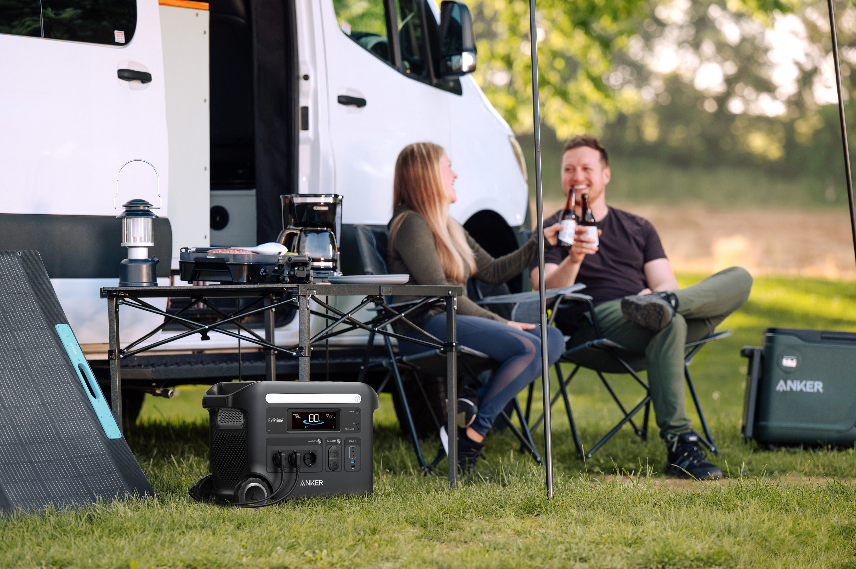Para relaksująca się w pobliżu vana, pijąca drinki. Widoczna jest stacja zasilania i sprzęt kempingowy.