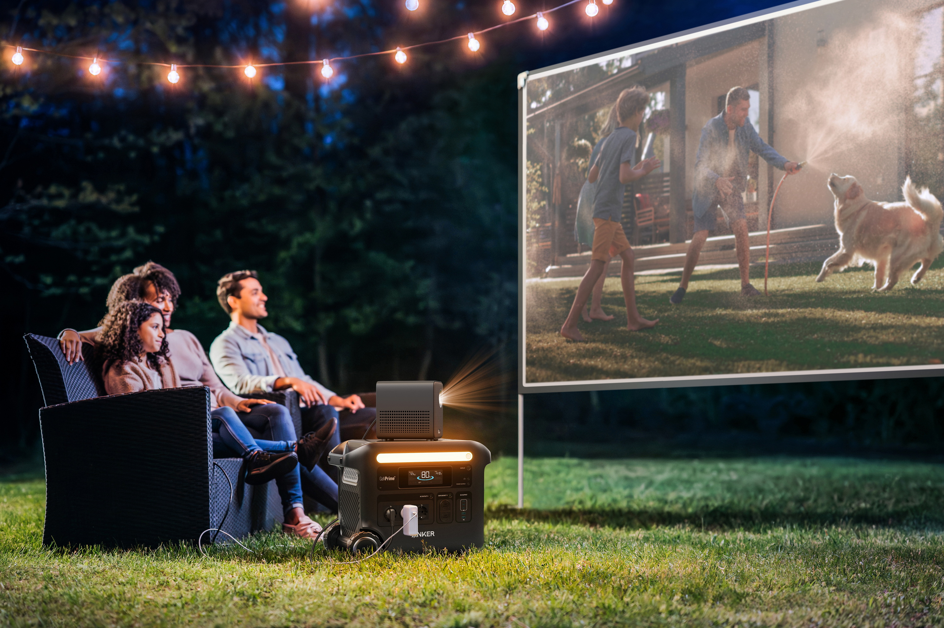 Grupa ludzi ogląda film wyświetlany na ekranie na podwórku. Pies bawi się wodą.