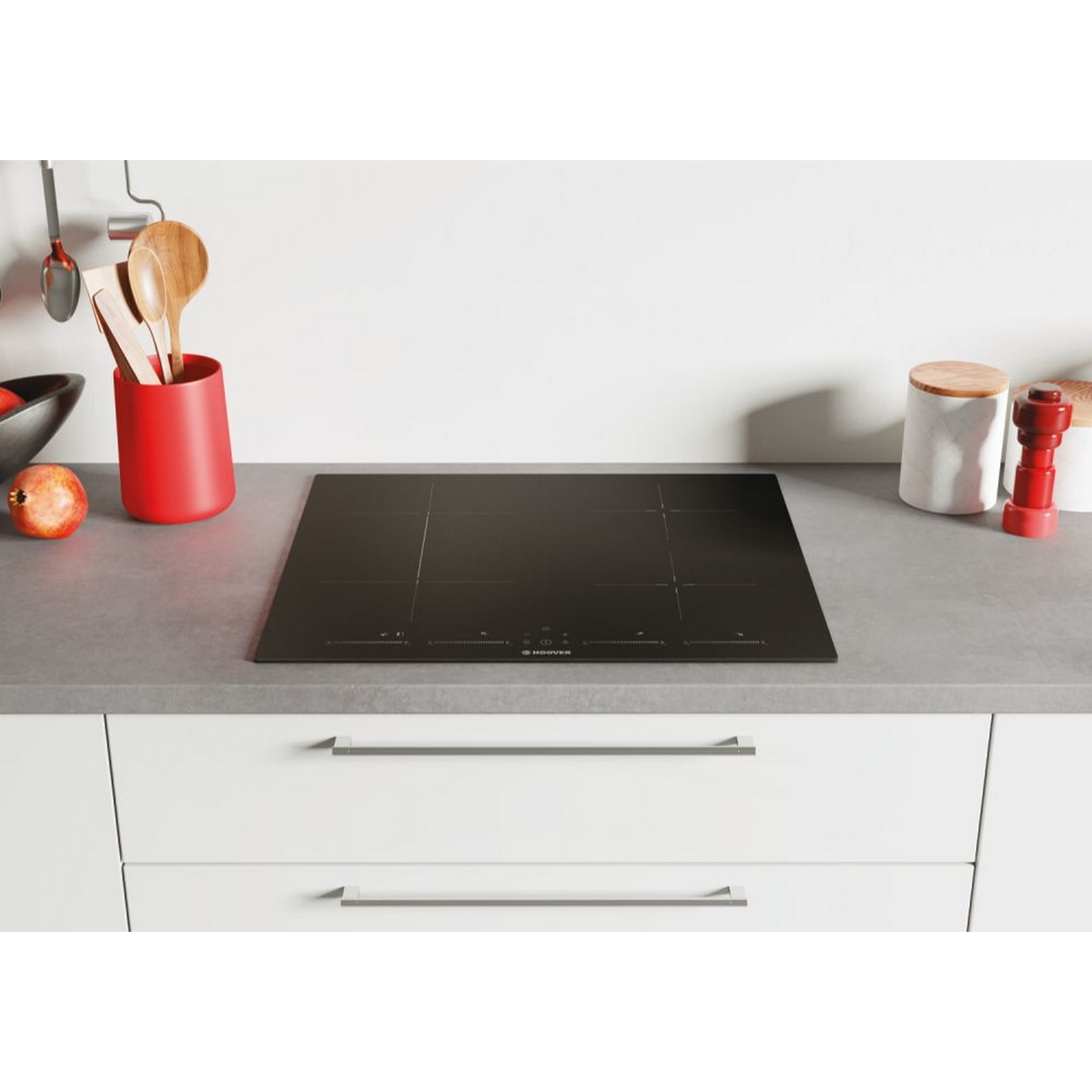 Un piano cottura a induzione nero con un piano di lavoro e armadi bianchi. Altri oggetti da cucina sono visibili.