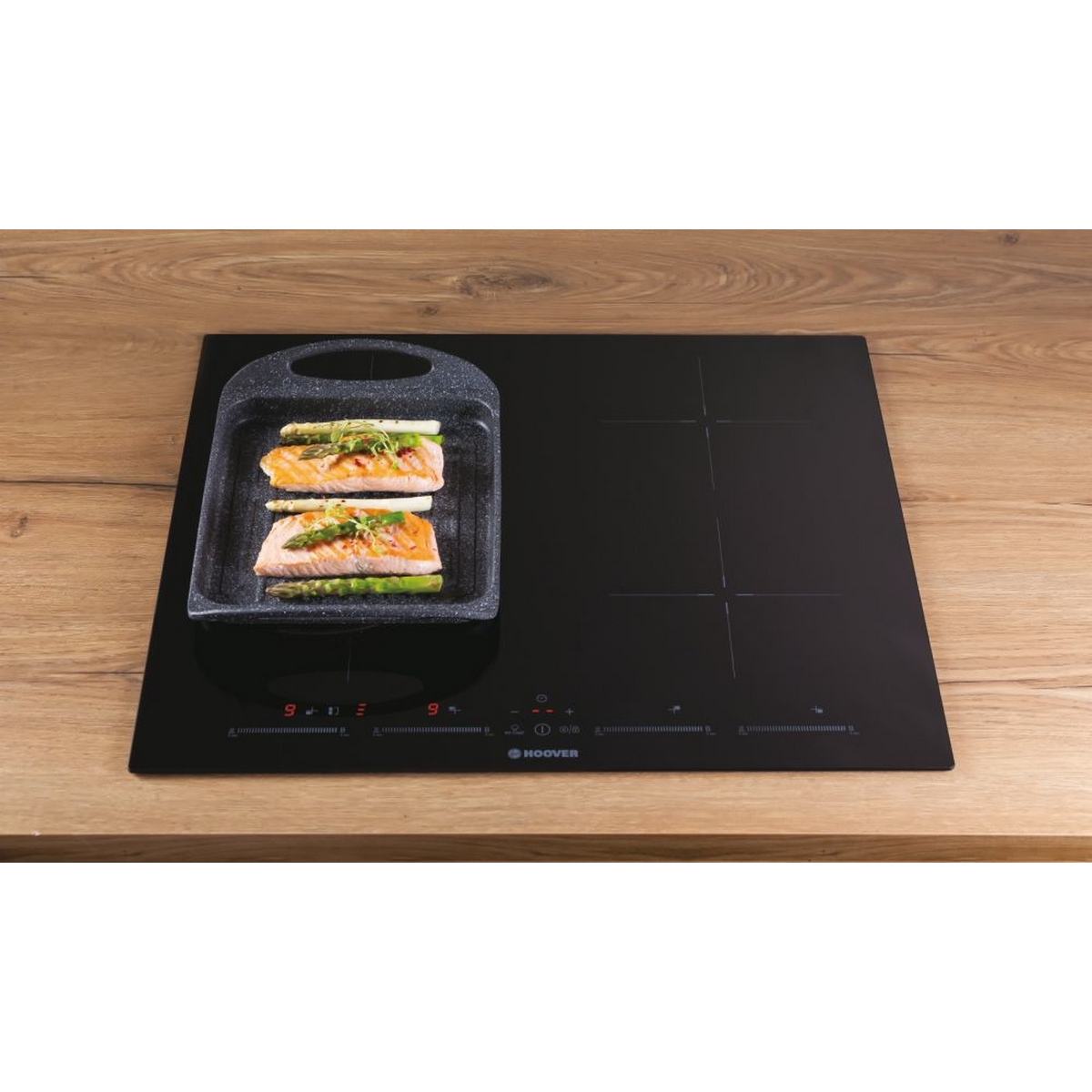 Piano cottura nero con una piastra e salmone. Superficie in legno e marchio Hoover.