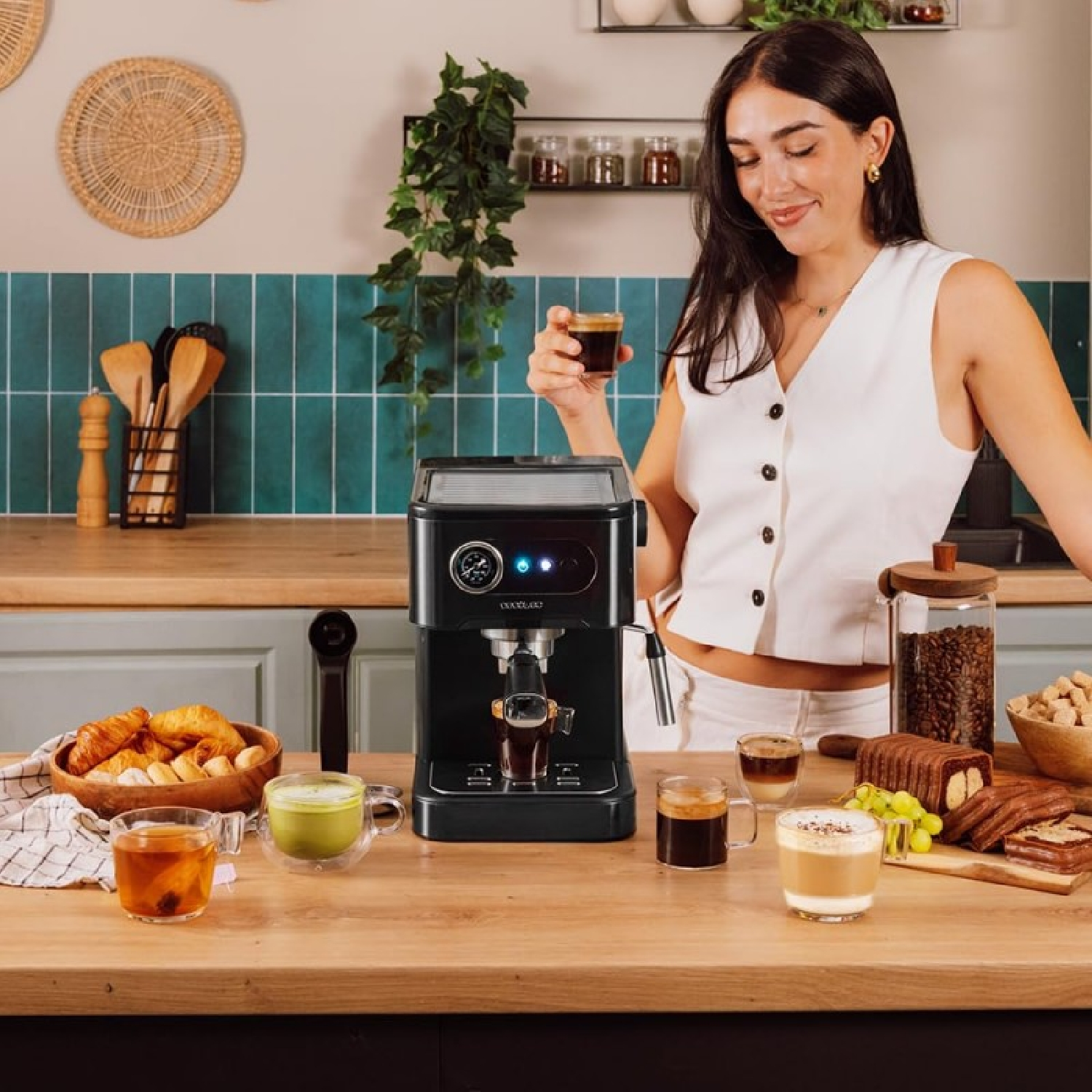Frau mit Kaffee, Espressomaschine und verschiedenen Lebensmitteln auf einer Holzplatte in einer Küche.