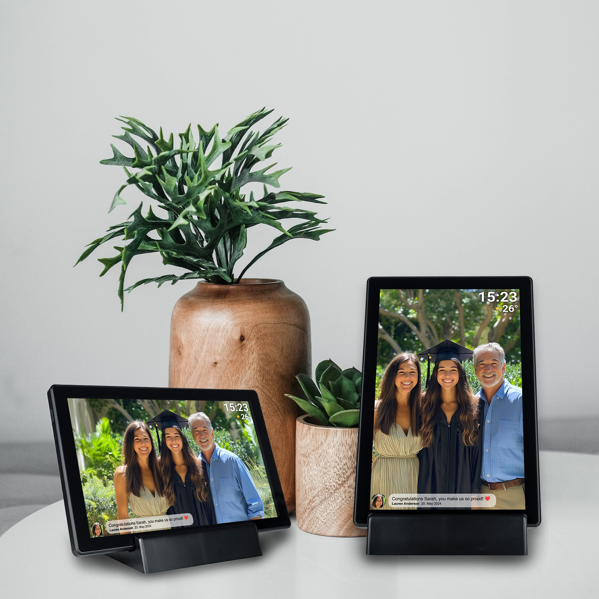 Two digital photo frames displaying graduation photos, with a plant and wooden vase in the background.