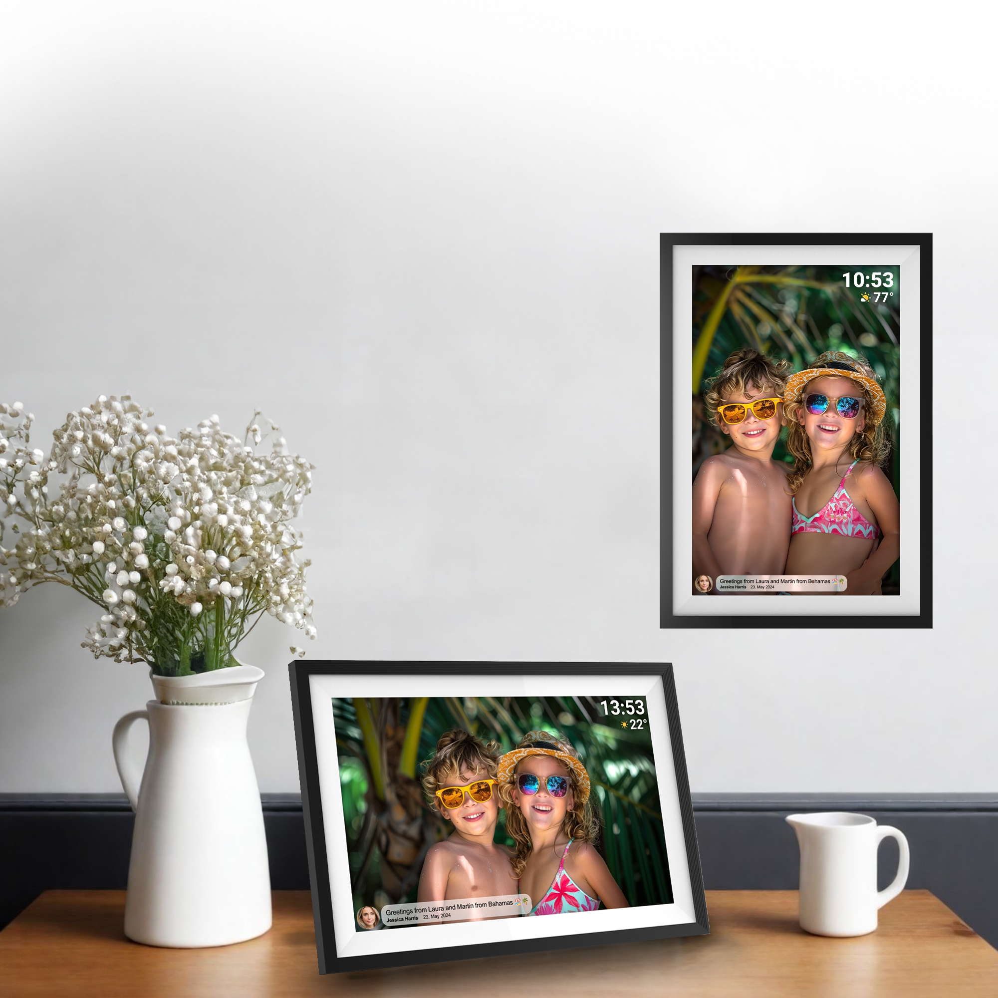 Deux cadres photo numériques avec photos d'enfants sur un mur blanc avec fleurs et pichet.