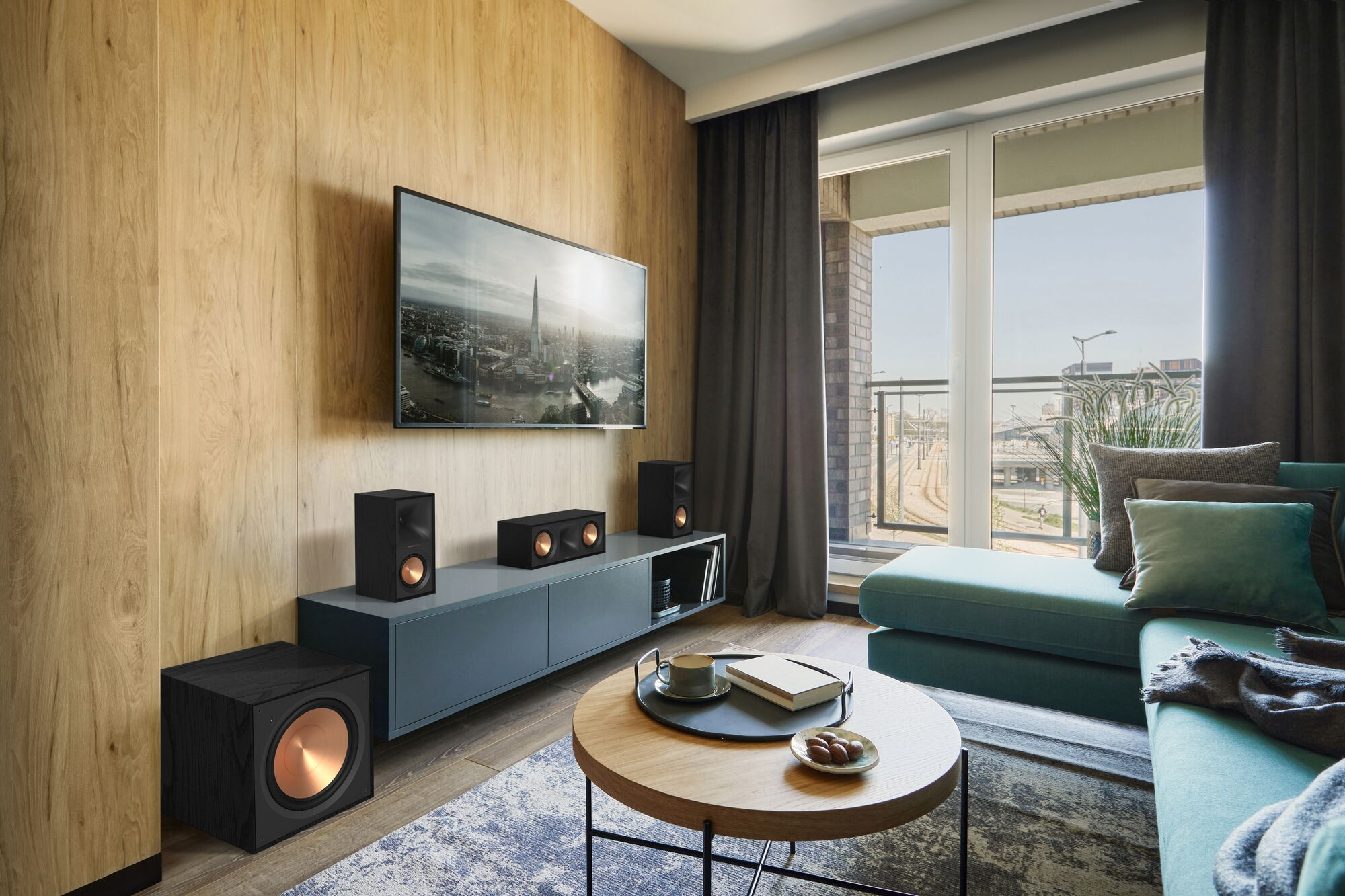 Ein Wohnzimmer mit Holzwänden, einem Fernseher, Lautsprechern, einem Sofa und einem runden Couchtisch.