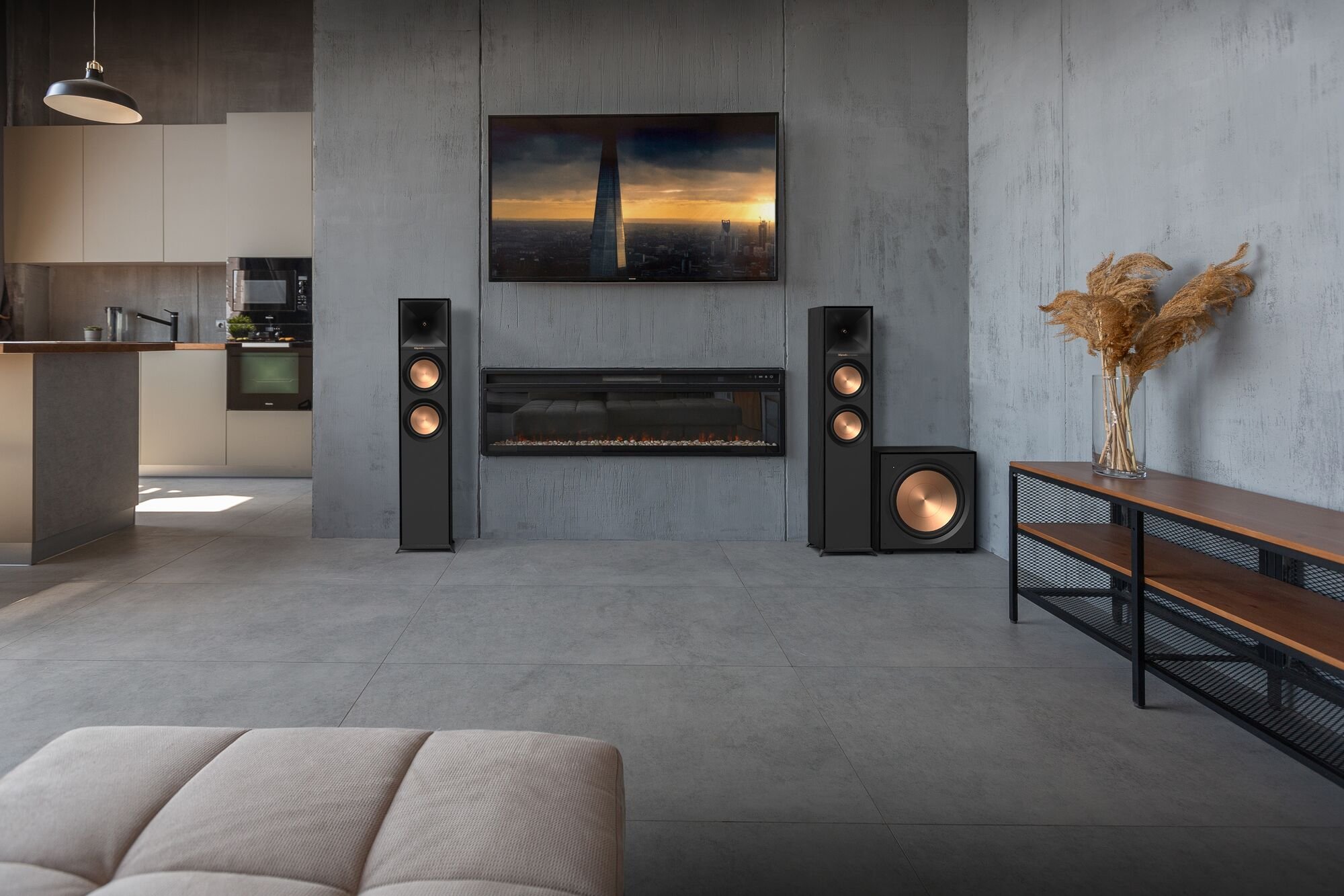 Wohnzimmer mit Lautsprechern, TV und Kamin. Braunes Sofa und Vase mit Pampasgras.