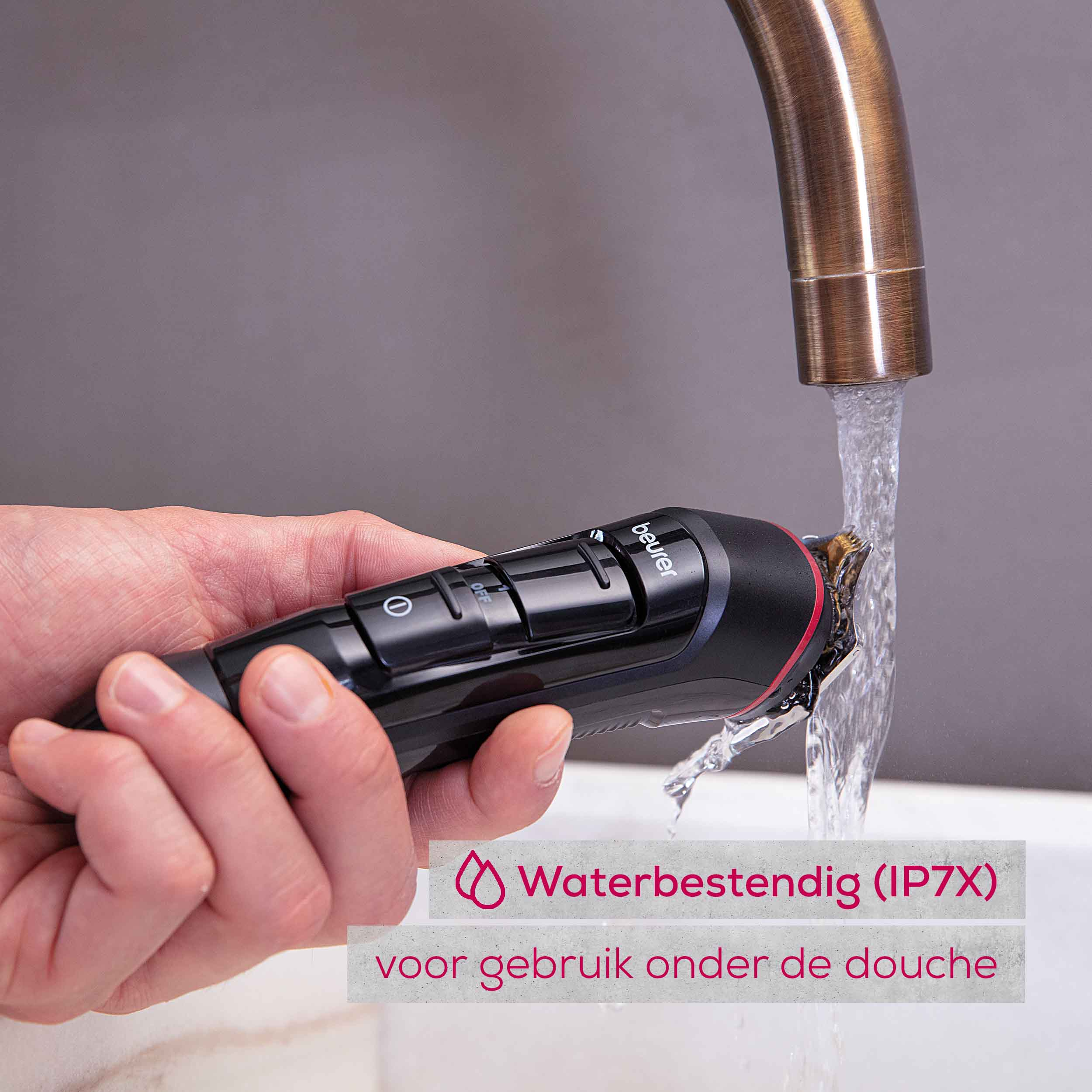 Een zwarte en rode elektrische trimmer die onder stromend water wordt gebruikt, met zichtbare waterdruppels.
